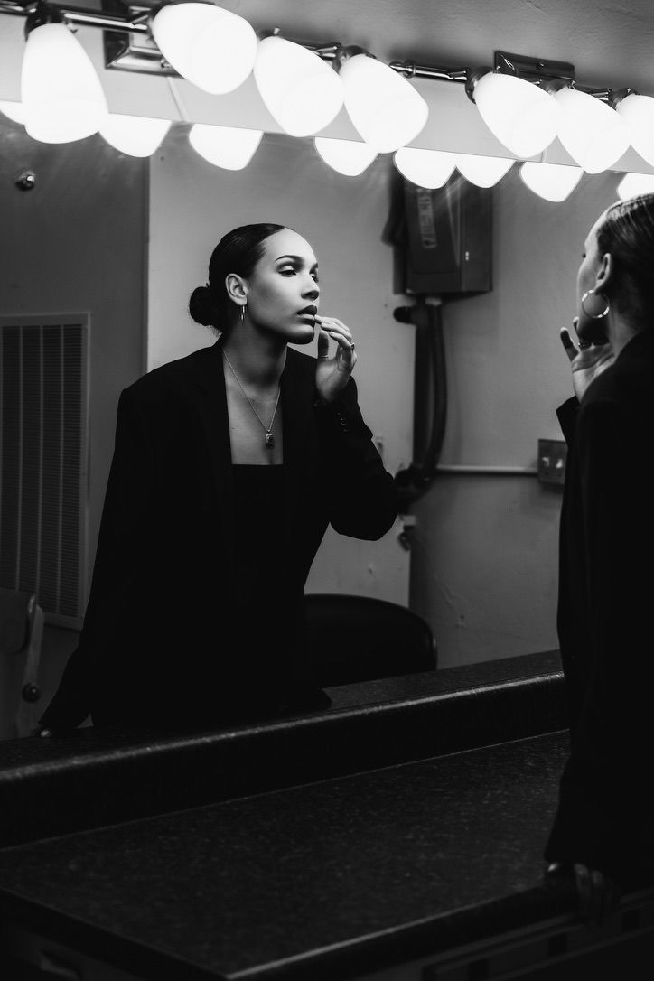 Black and white photo of a woman applying lipstick in a dressing room mirror with Hollywood lights.