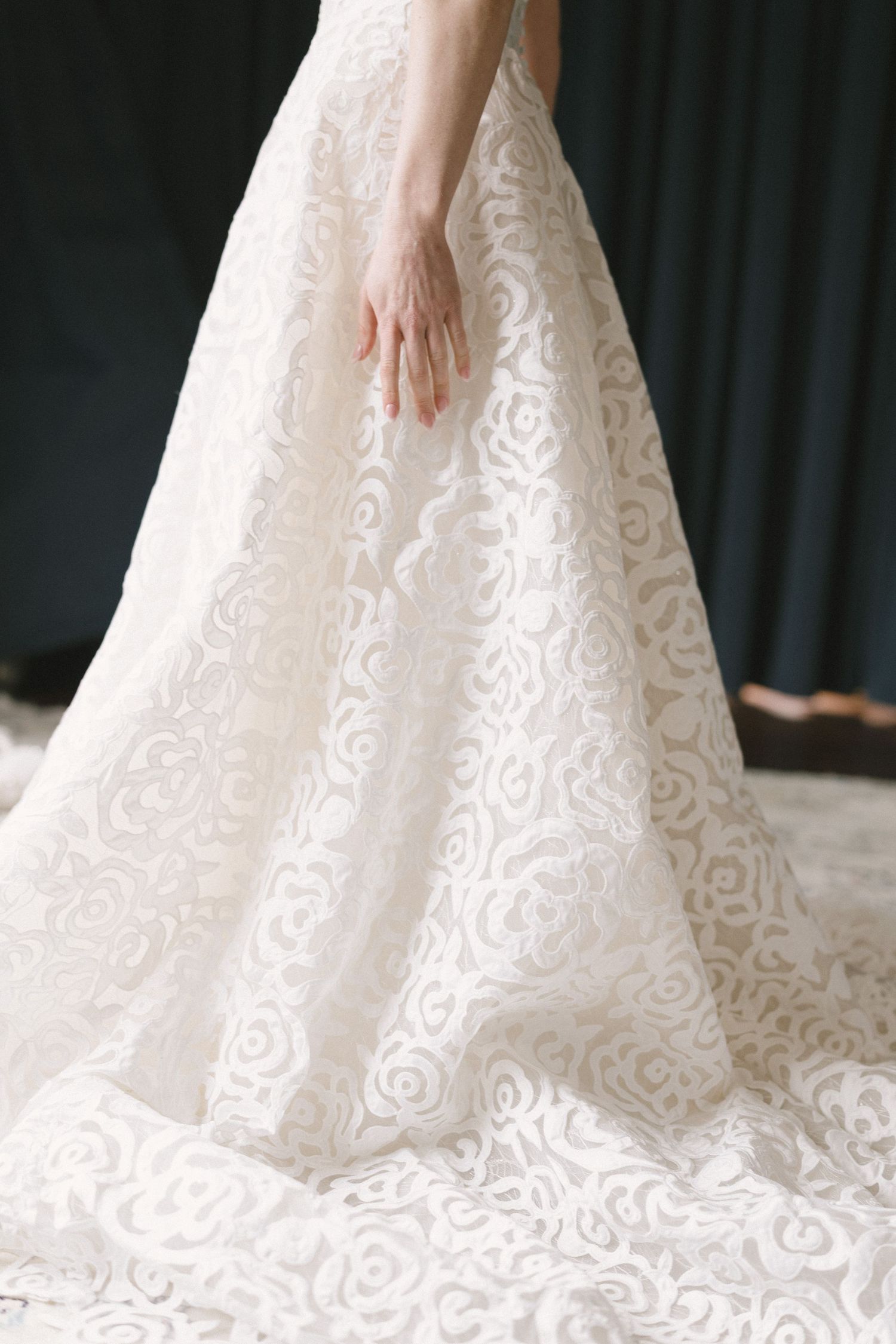 Close-up view of an elegant white lace wedding dress with intricate floral patterns trailing along the floor.