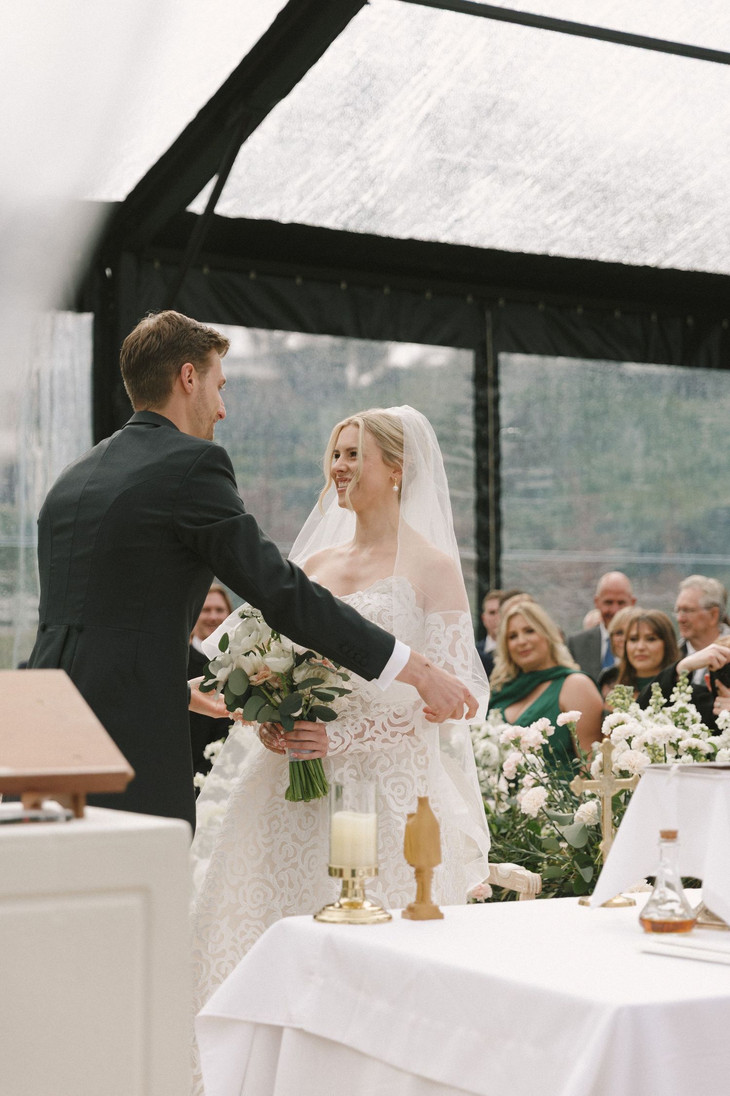 A wedding couple shares a tender moment at their reception table decorated with white linens and floral arrangements.