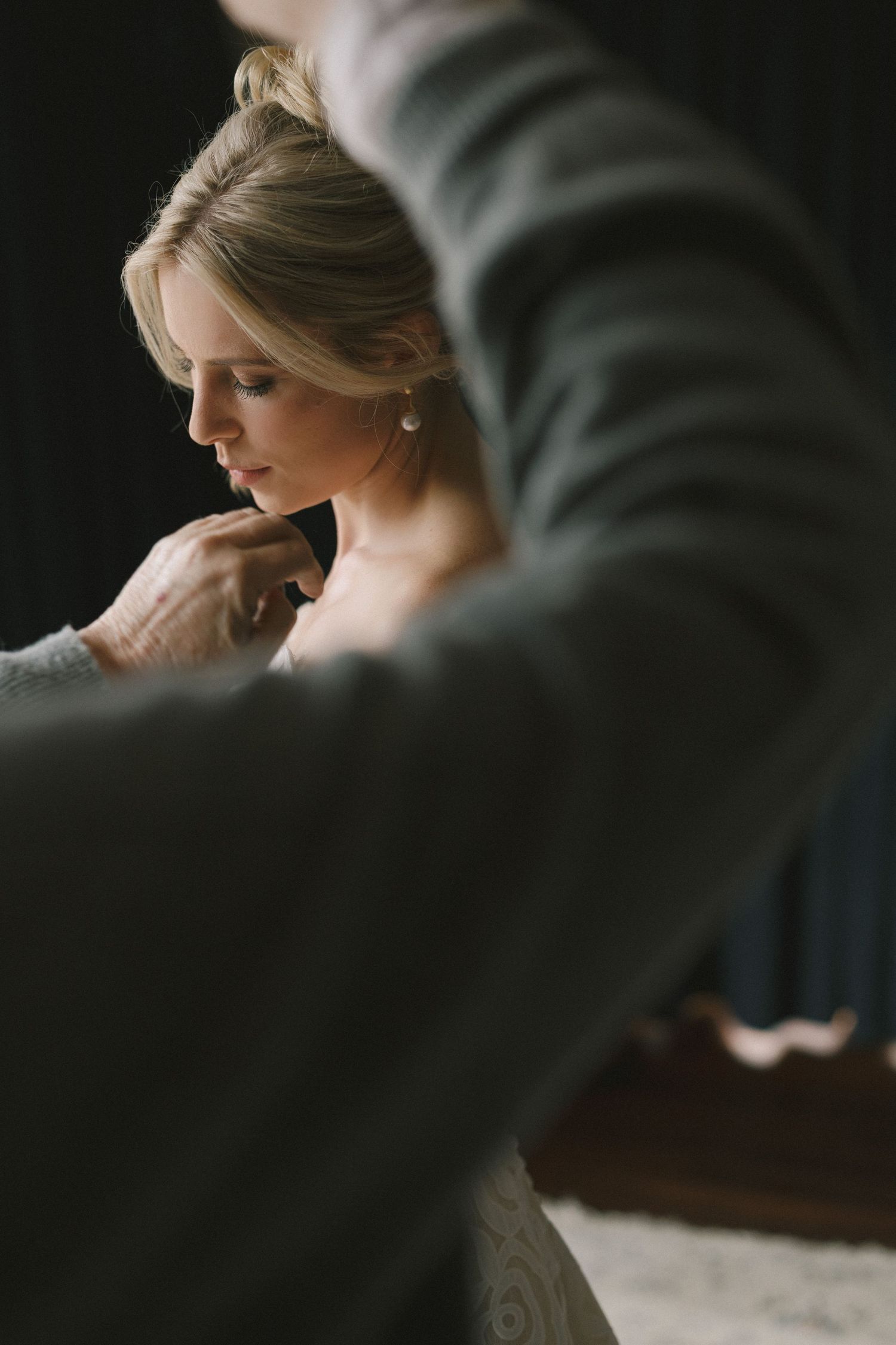 Final preparations and styling touches being made in an intimate, moody setting with soft lighting and elegant details.