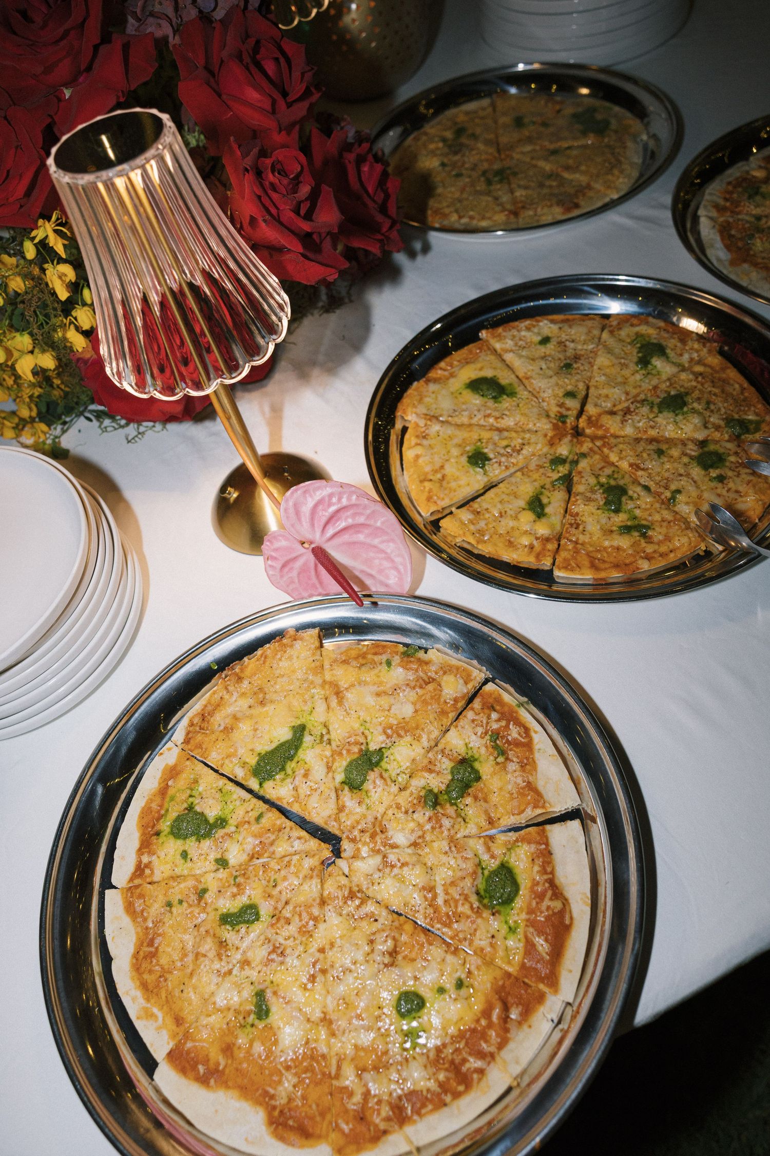 Two sliced pizzas topped with fresh basil and cheese served on silver trays at an elegant dinner party setting.