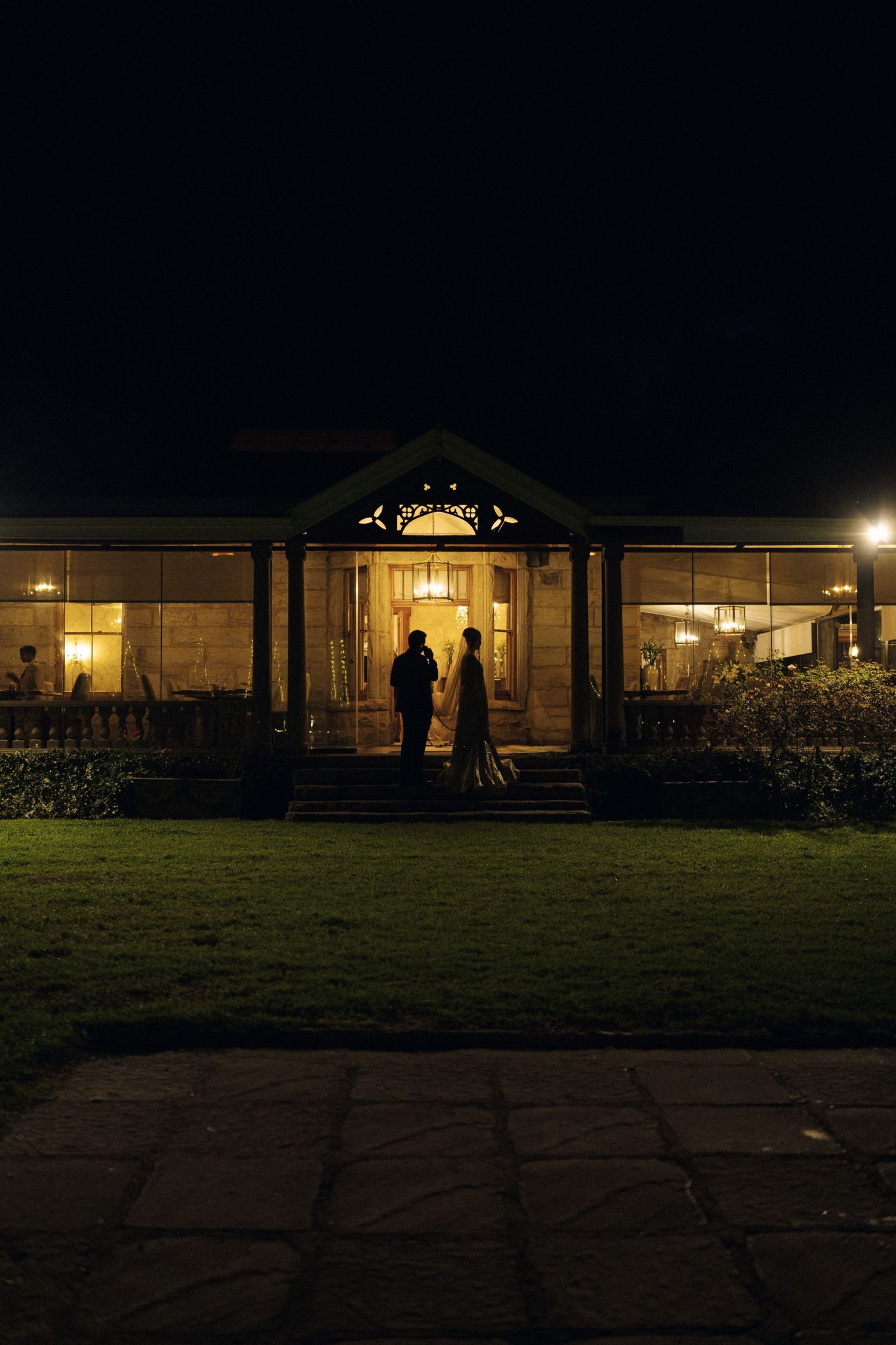 Couple silhouetted against illuminated colonial venue facade at night during wedding reception.