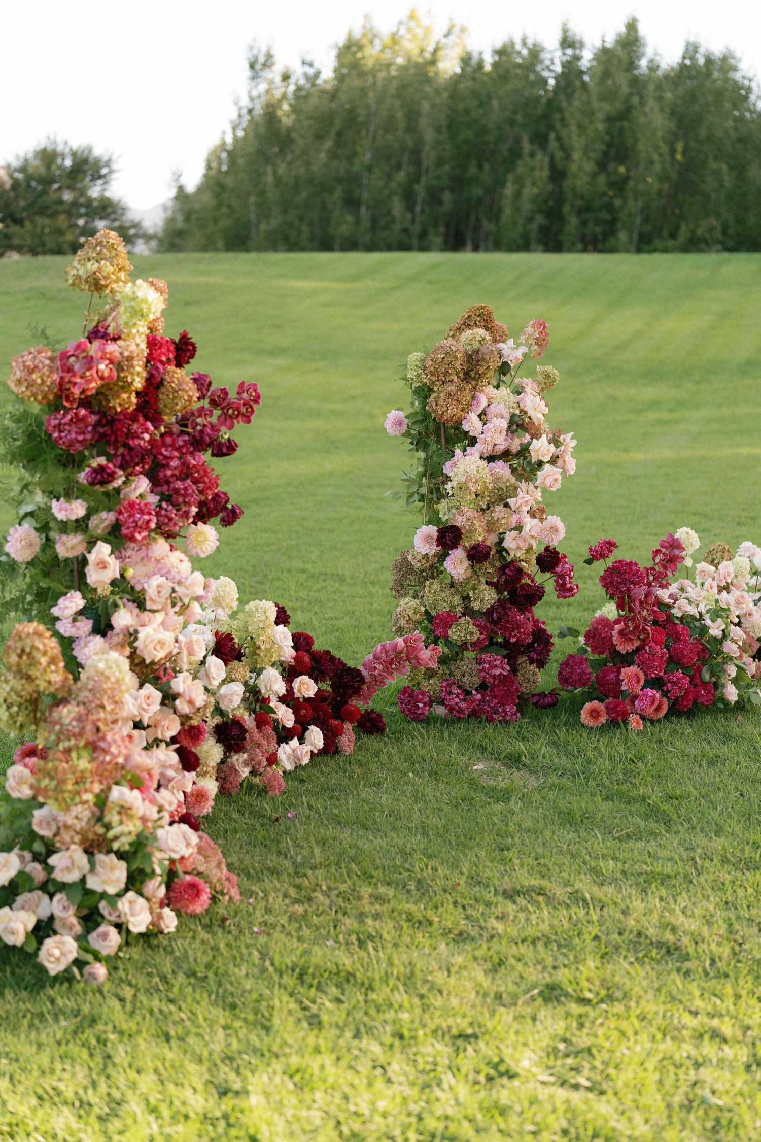Romantic floral installation with burgundy and blush roses arranged in organic clusters on a grassy lawn.