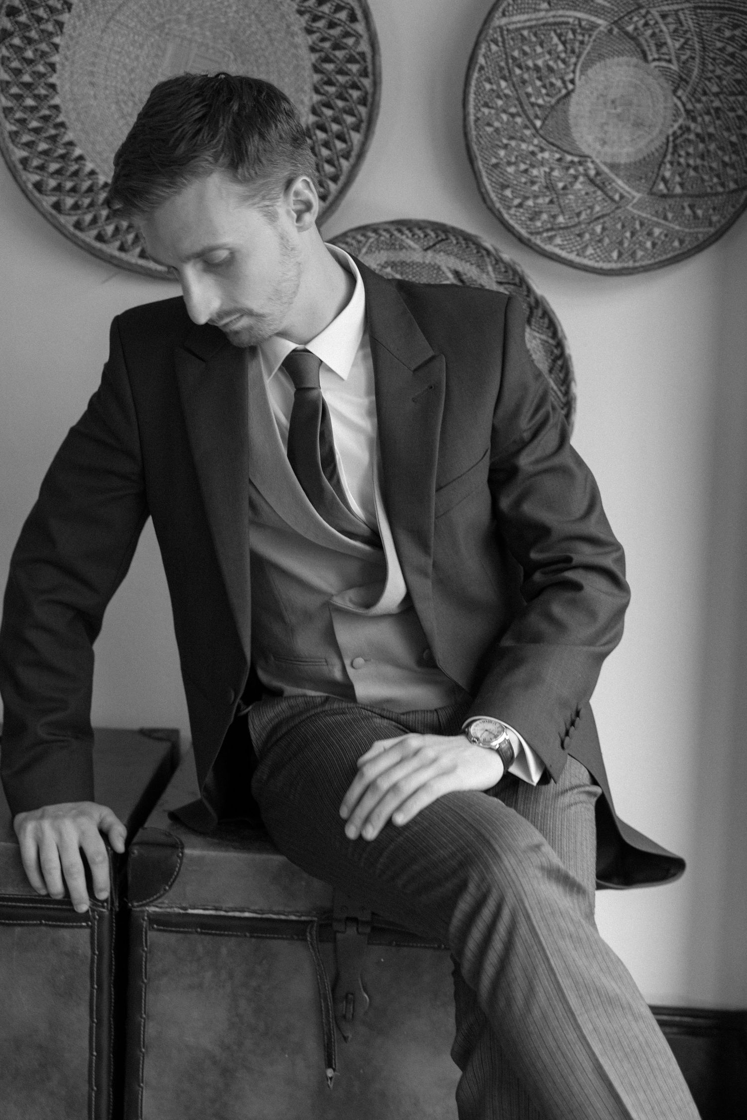 A black and white photo shows a person in a business suit sitting in contemplative poses against a textured wall.