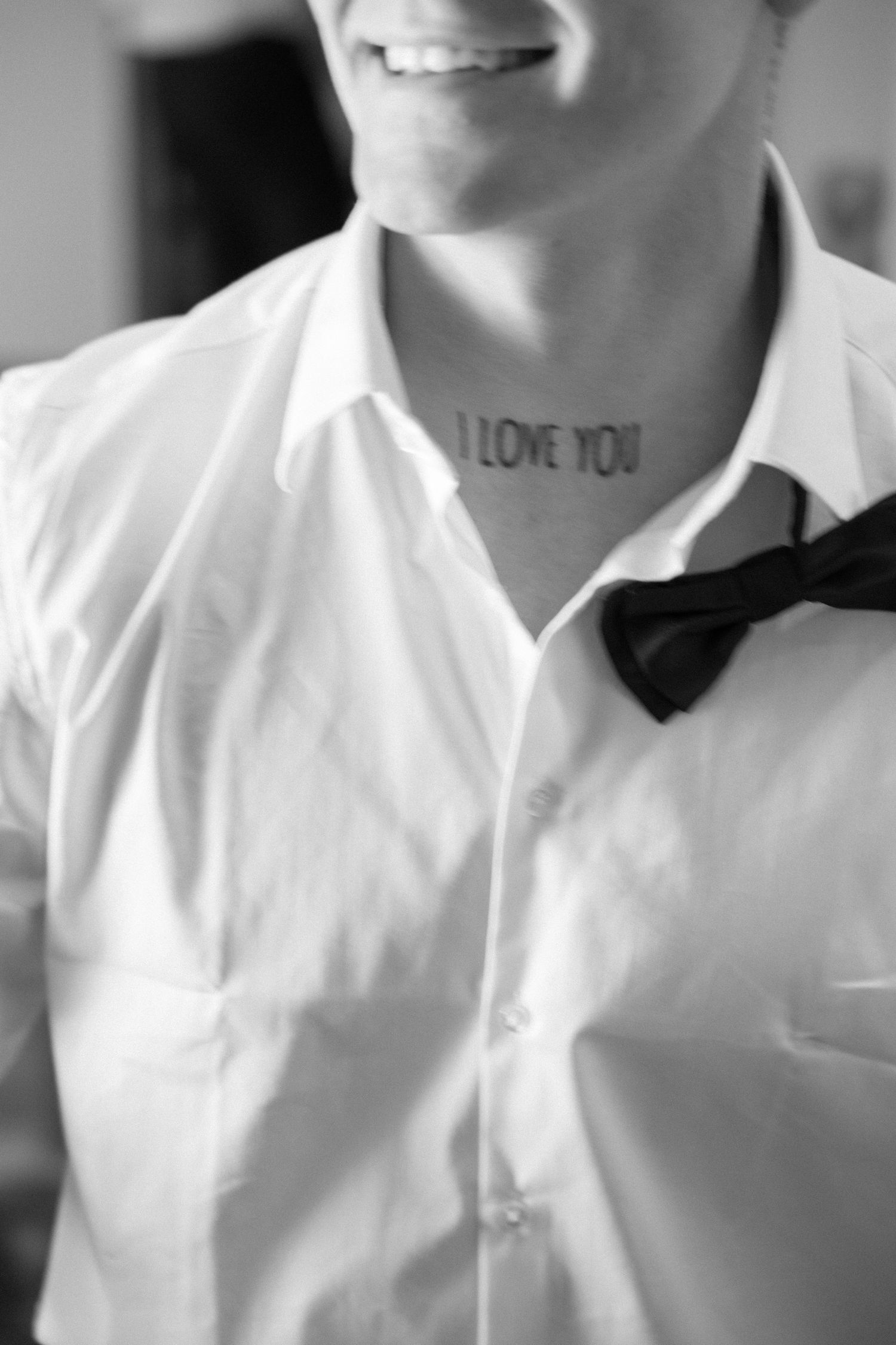 Person wearing a crisp white button-down shirt with a black bow tie detail smiles warmly at the camera.