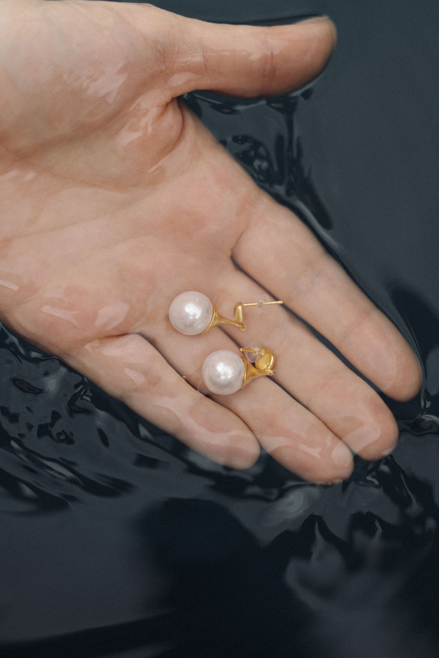 Hand holding two elegant pearl rings against a dark reflective surface.