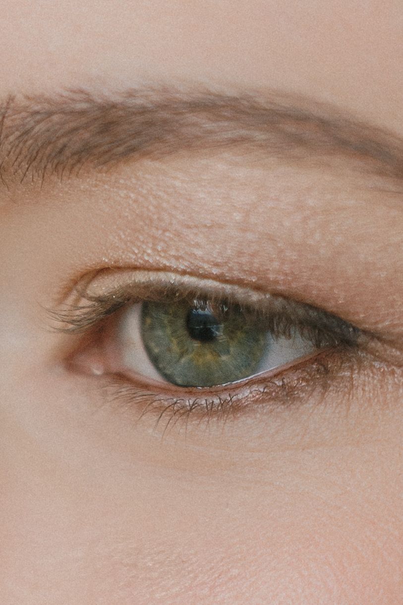 Close-up macro shot of a green eye with subtle eyeliner and natural eyebrow visible against pale skin.