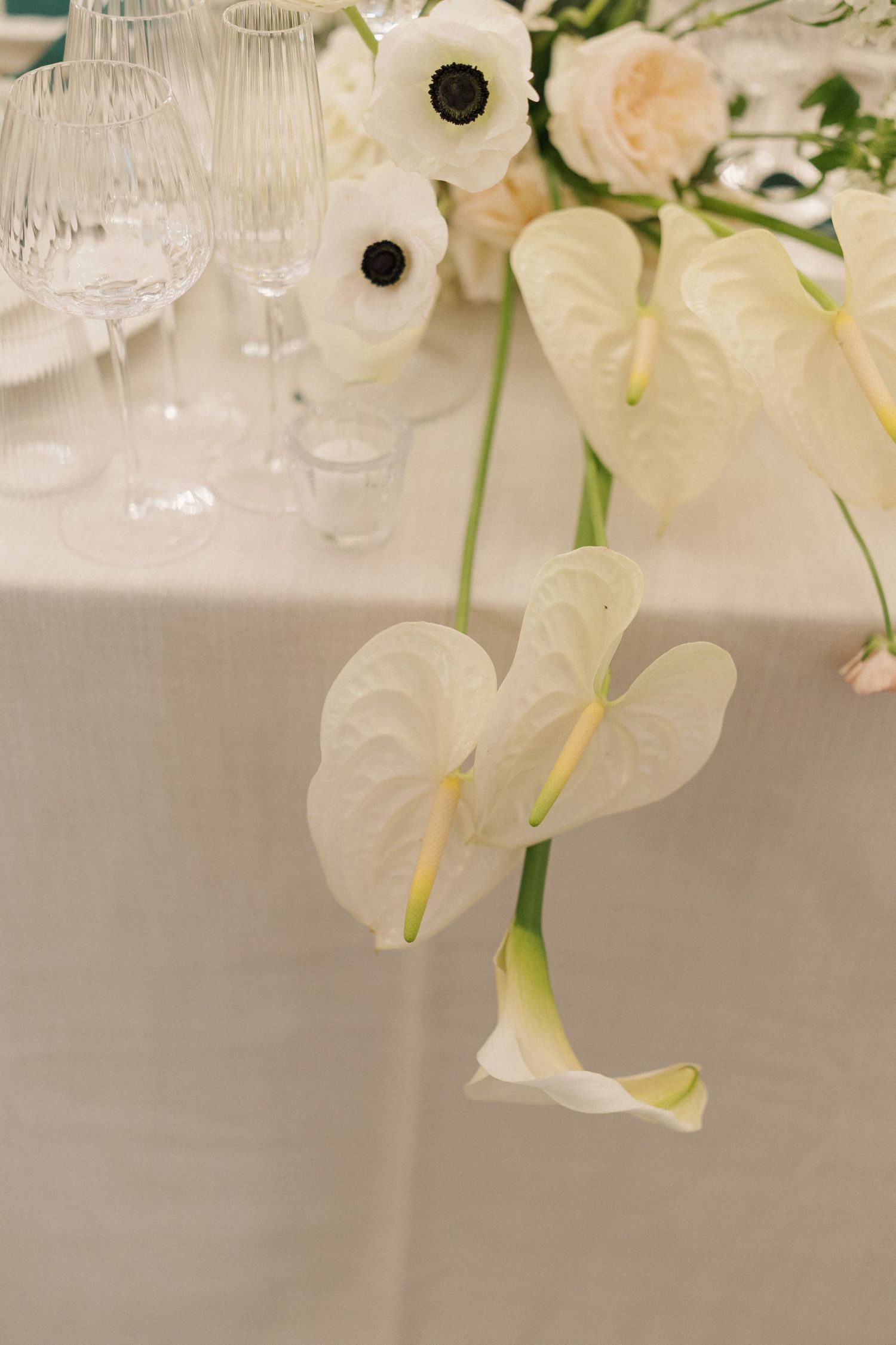 White calla lilies and wine glasses arranged elegantly on a white tablecloth for an upscale dining event.