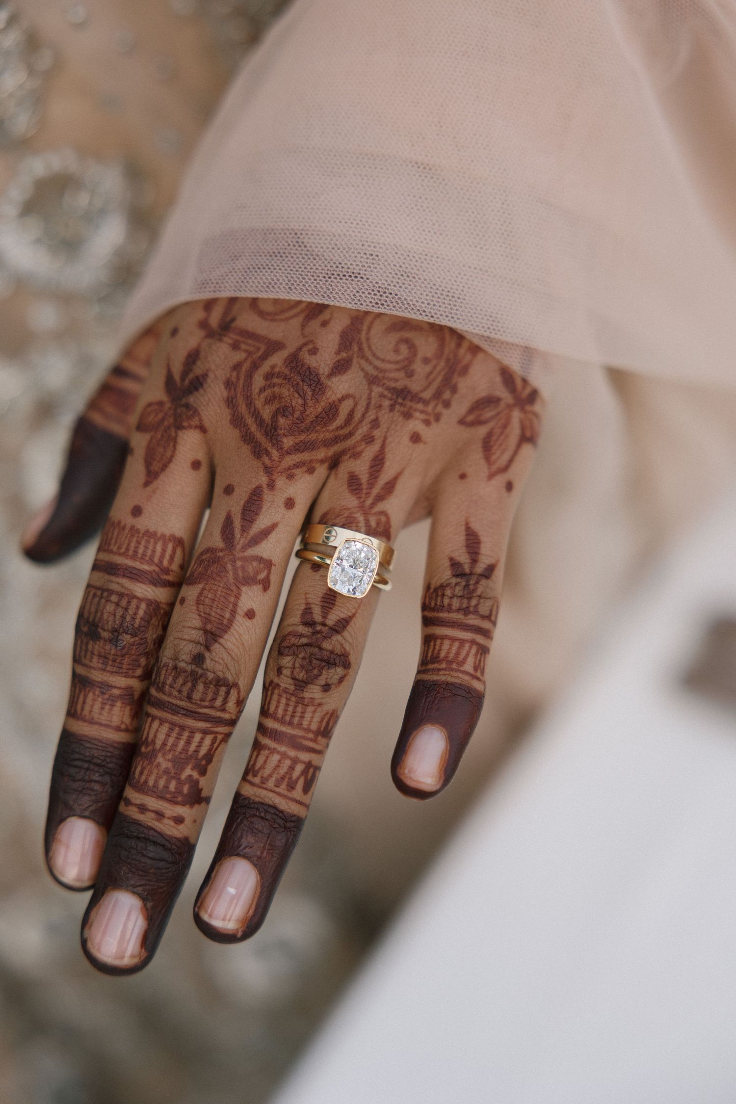 Close-up of bride's hand adorned with intricate henna mehndi design and large diamond engagement ring.