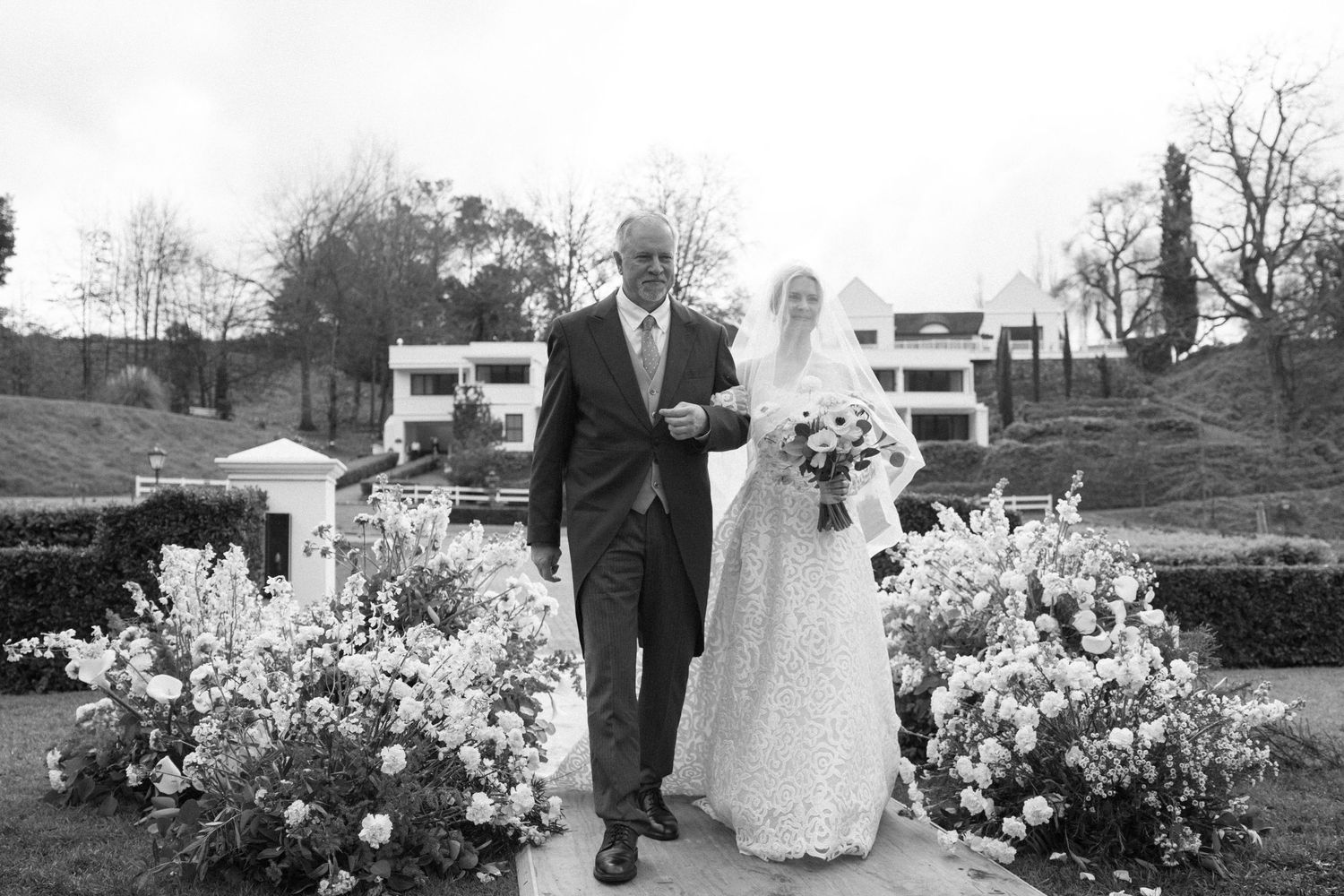 Black and white wedding photos show a couple in formal attire posing with floral arrangements outdoors.