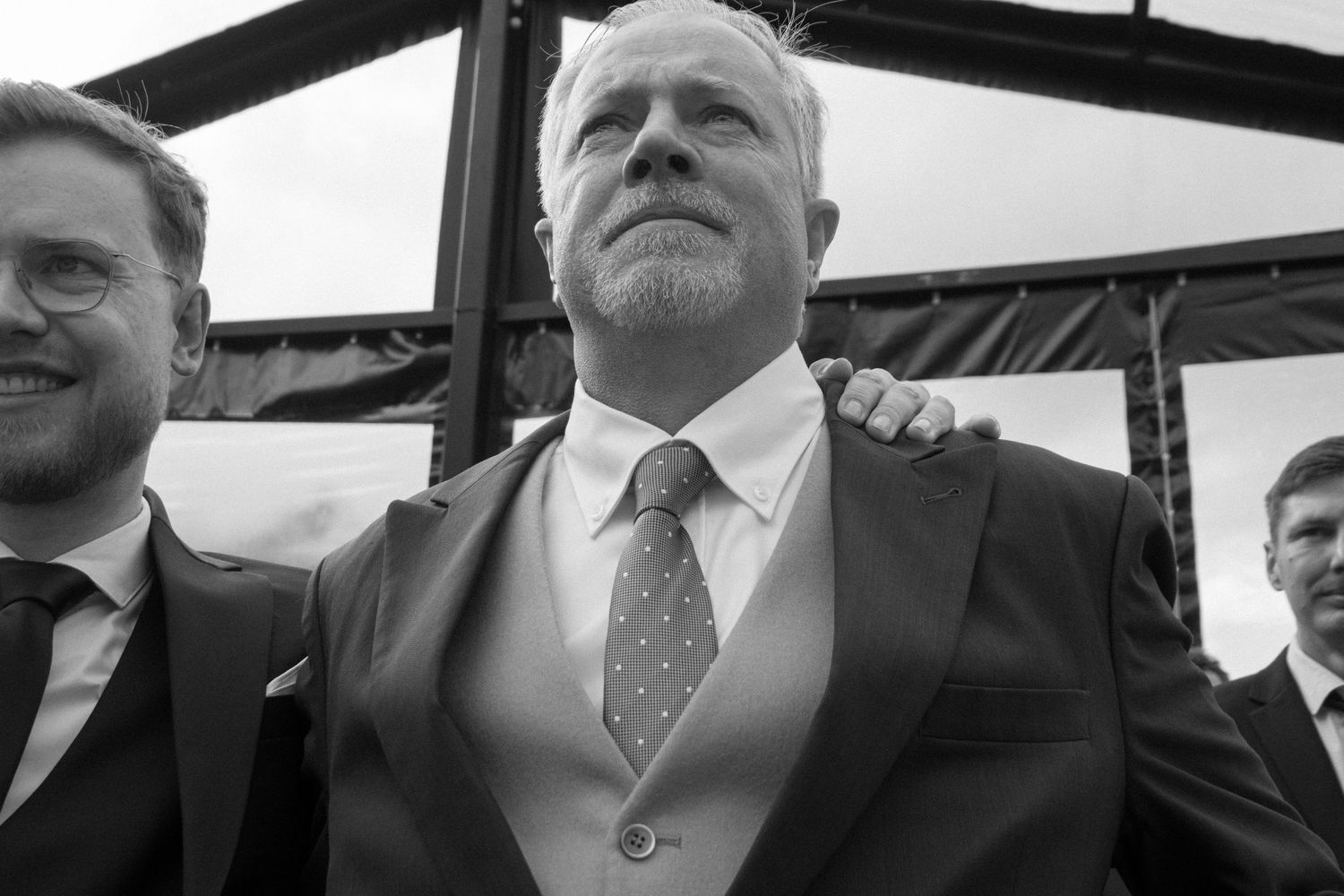 A black and white photo shows people in business attire standing together in what appears to be a covered walkway.