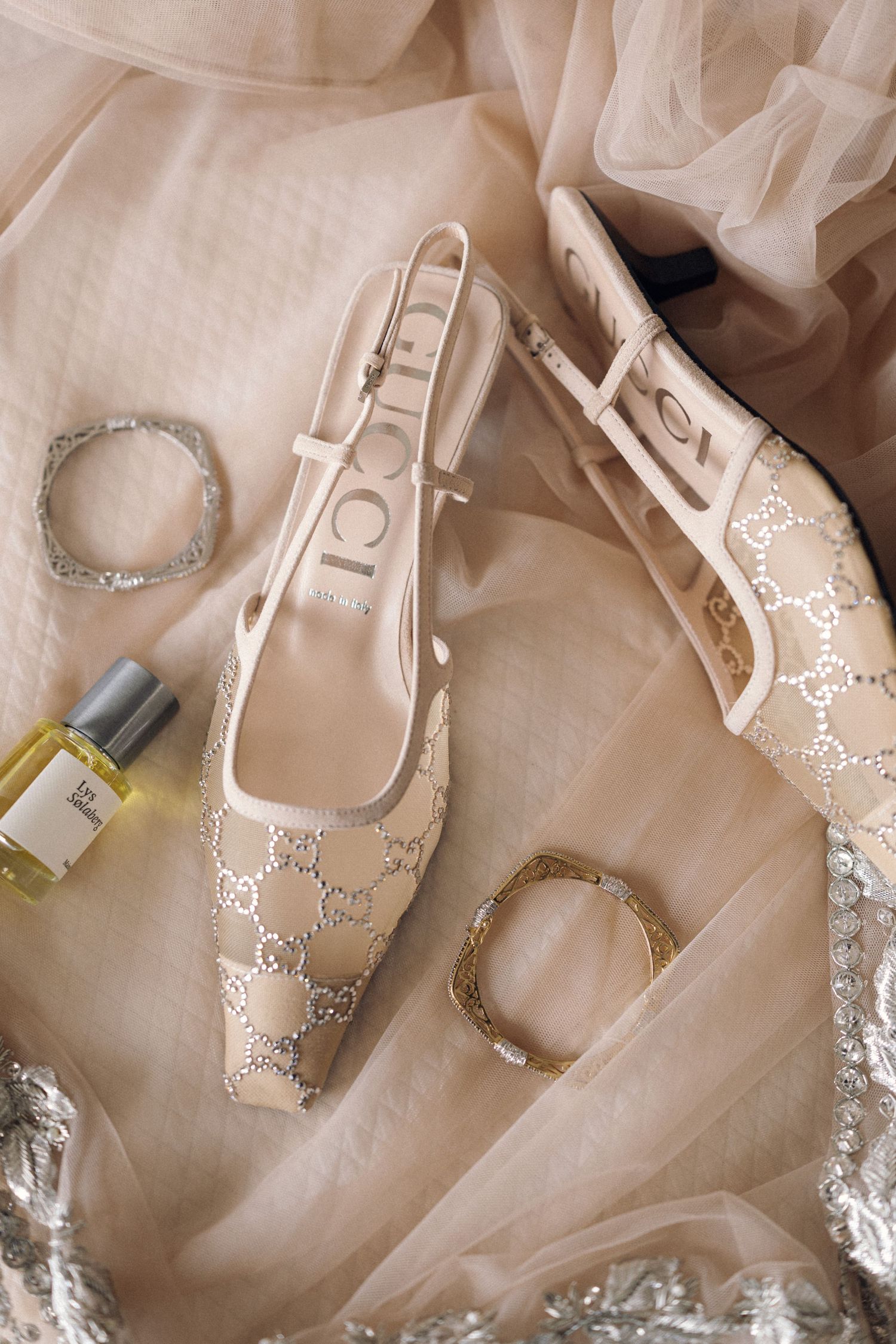 Gucci monogram slingback flats with silver bracelets and perfume bottle on beige tulle fabric.