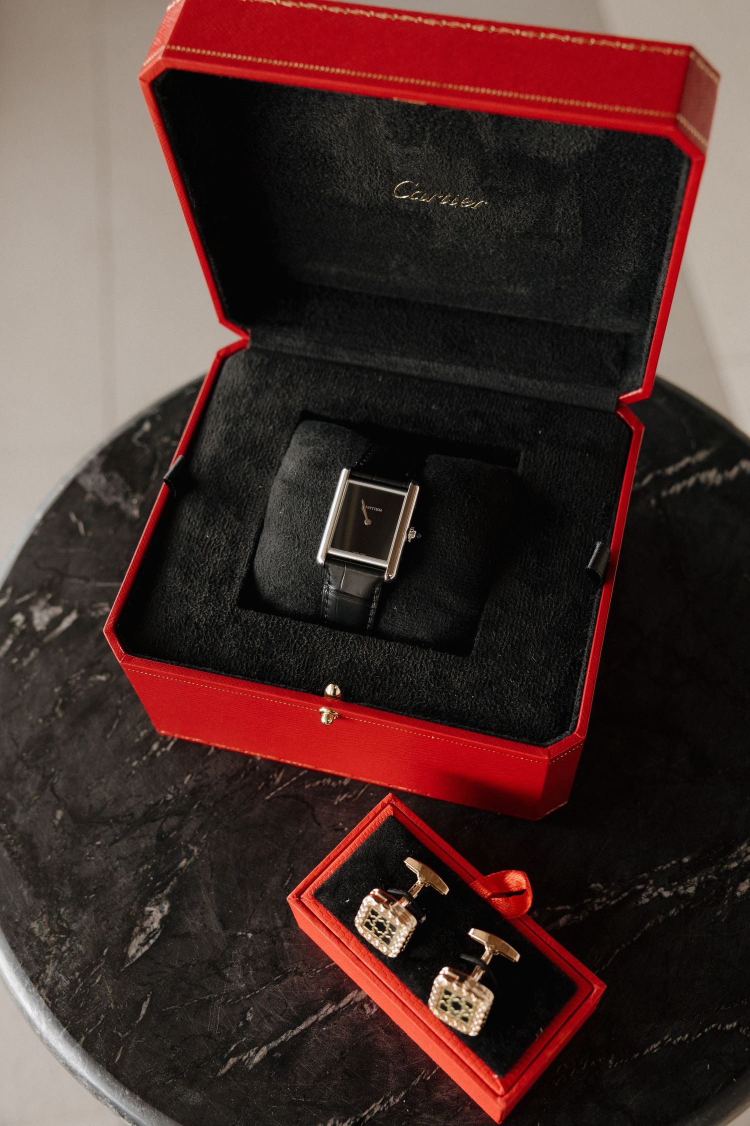 A red jewelry box with a black interior, containing a watch and earrings.