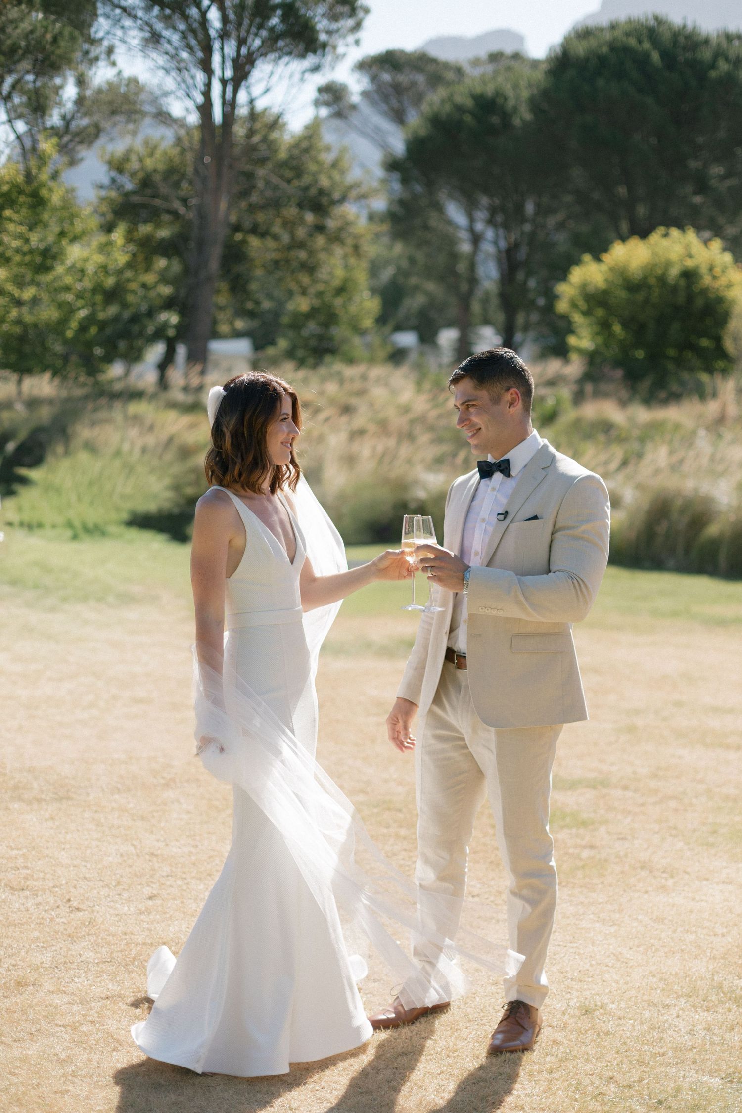 Couple in white wedding attire dancing and celebrating in sunny outdoor setting.