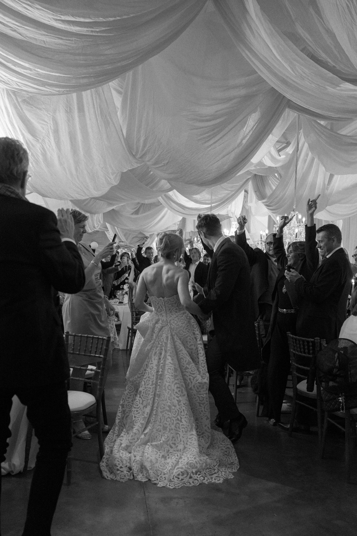Wedding guests dance and celebrate under an elegant white draped tent ceiling at an elegant reception.