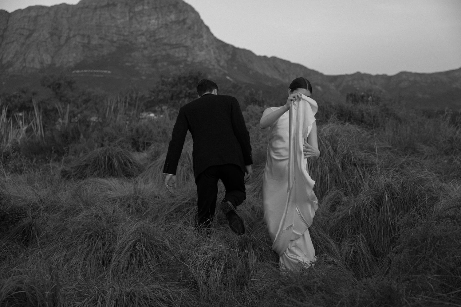 A black and white panoramic sequence showing figures walking through a mountainous desert landscape.