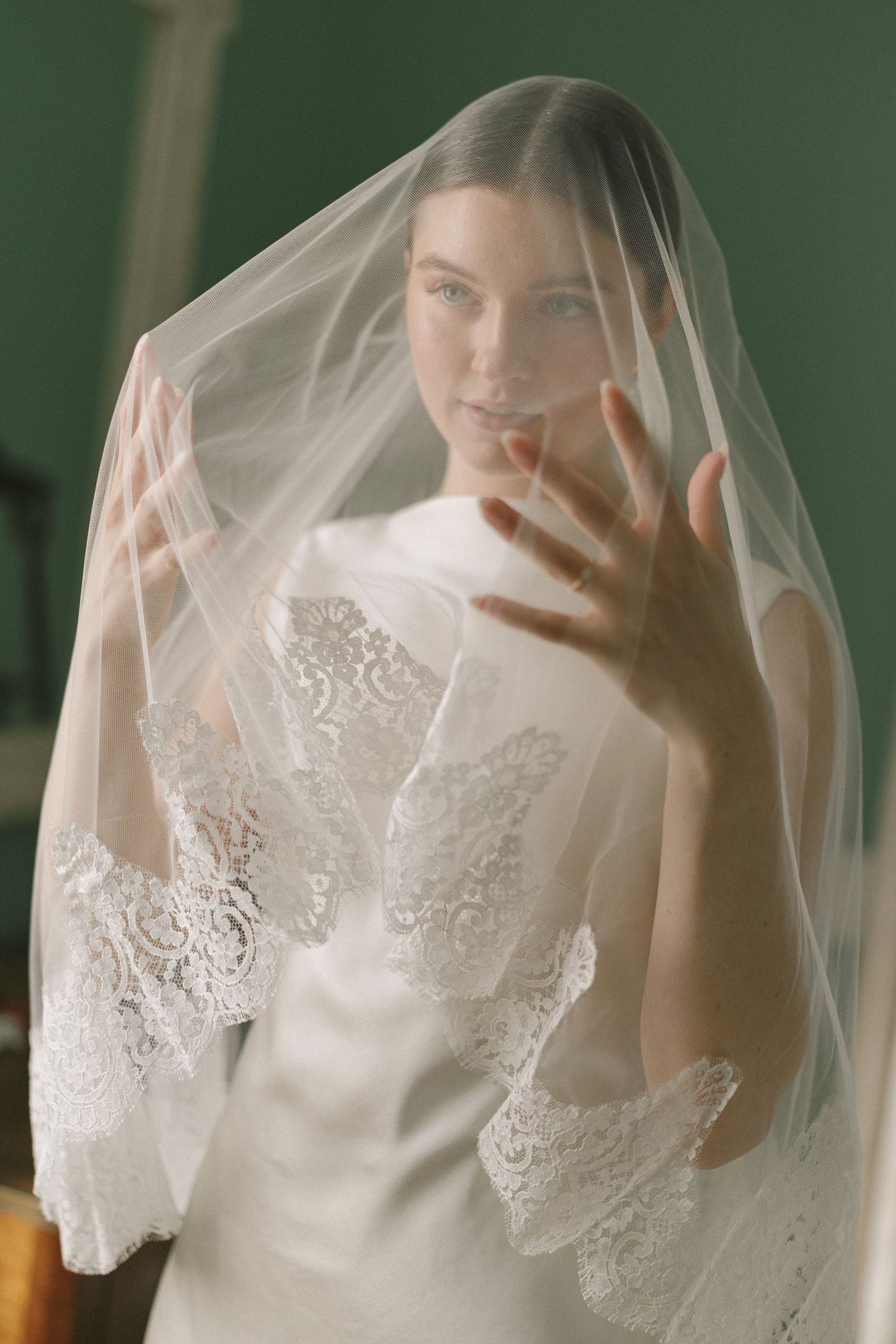 A bride wearing a delicate white lace veil poses in a series of ethereal portraits against a green background.
