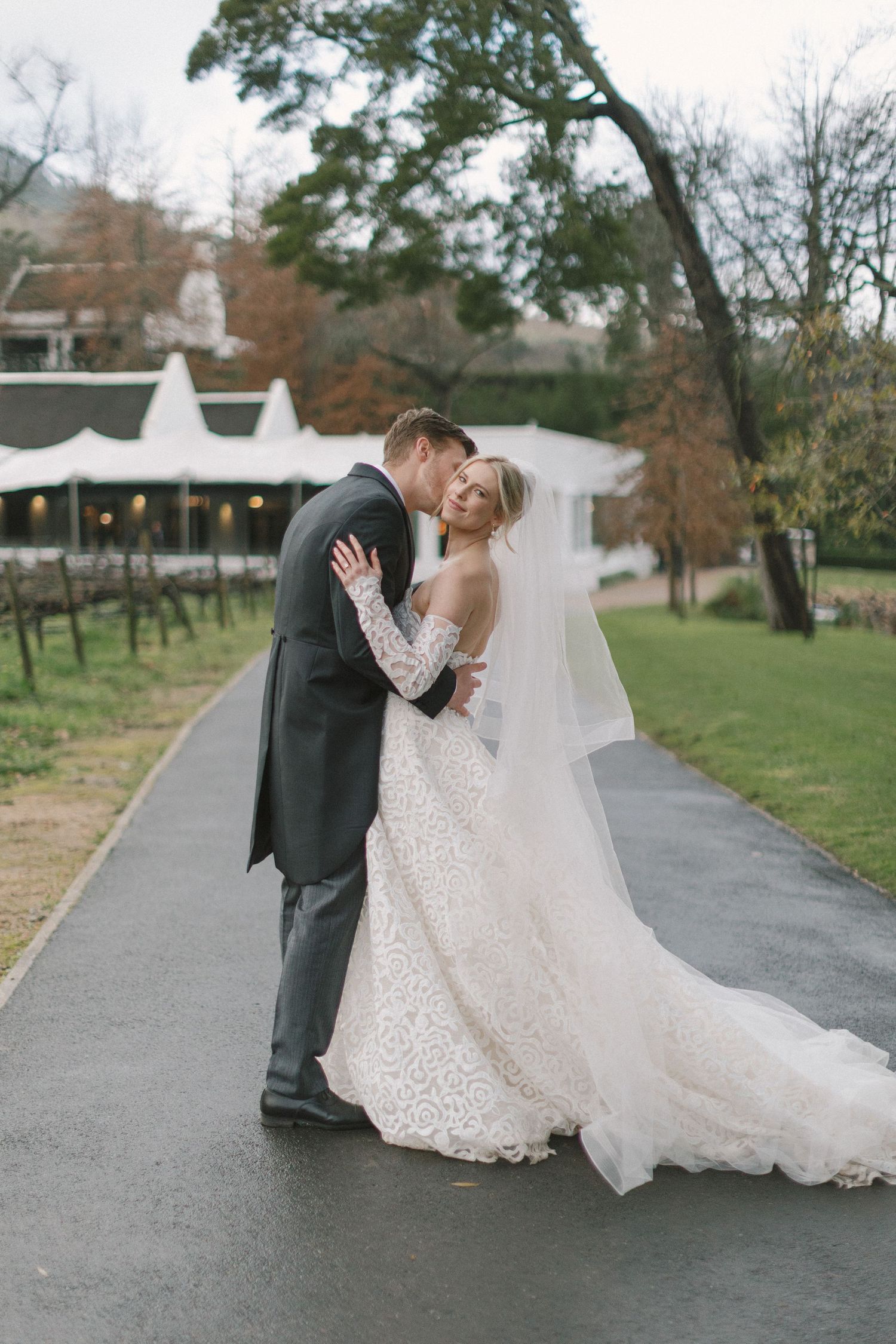 A romantic wedding couple shares intimate dance dips on a paved pathway surrounded by autumn trees.