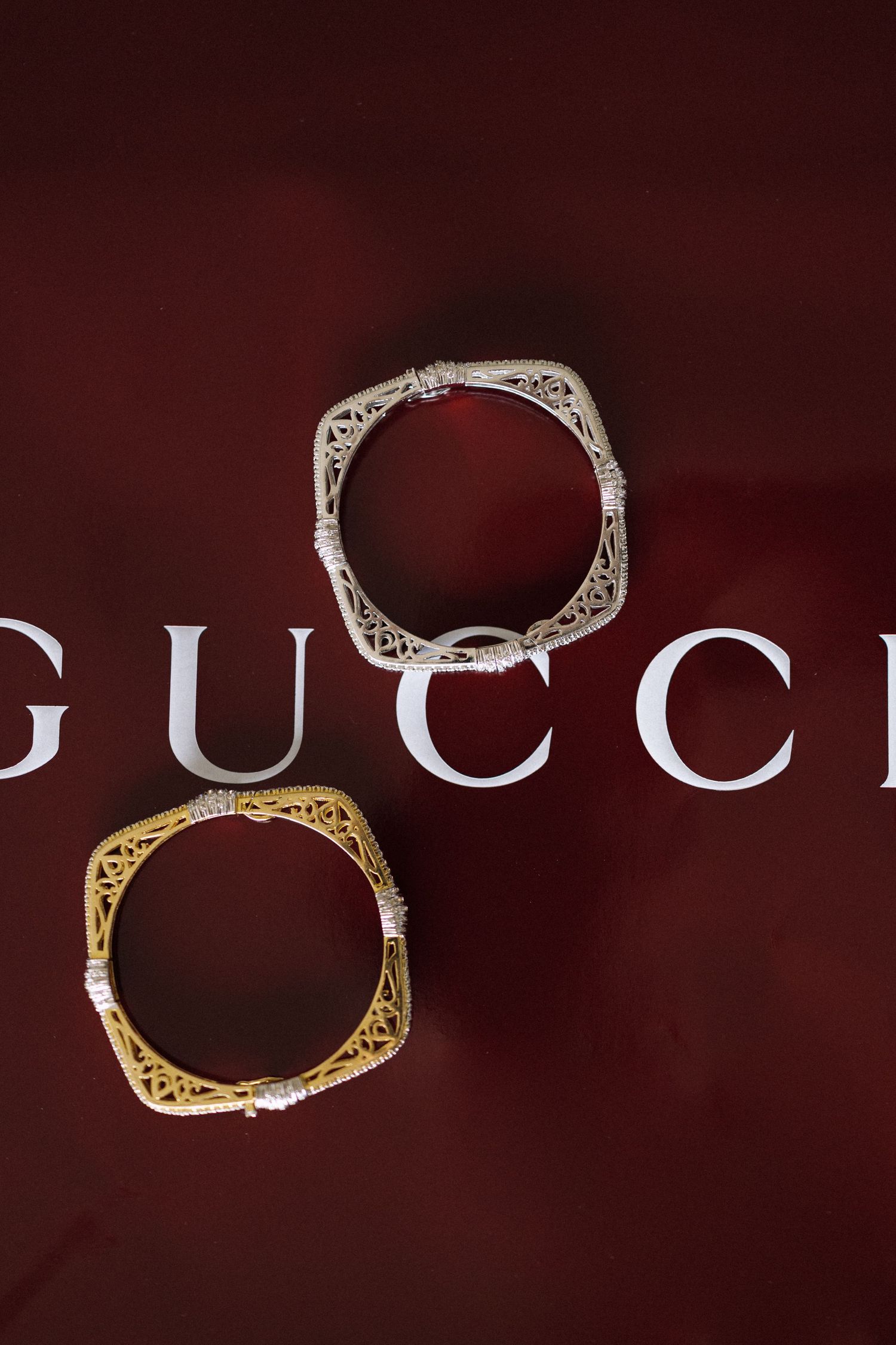 Three Gucci bamboo bracelets in gold and silver displayed on dark red background.