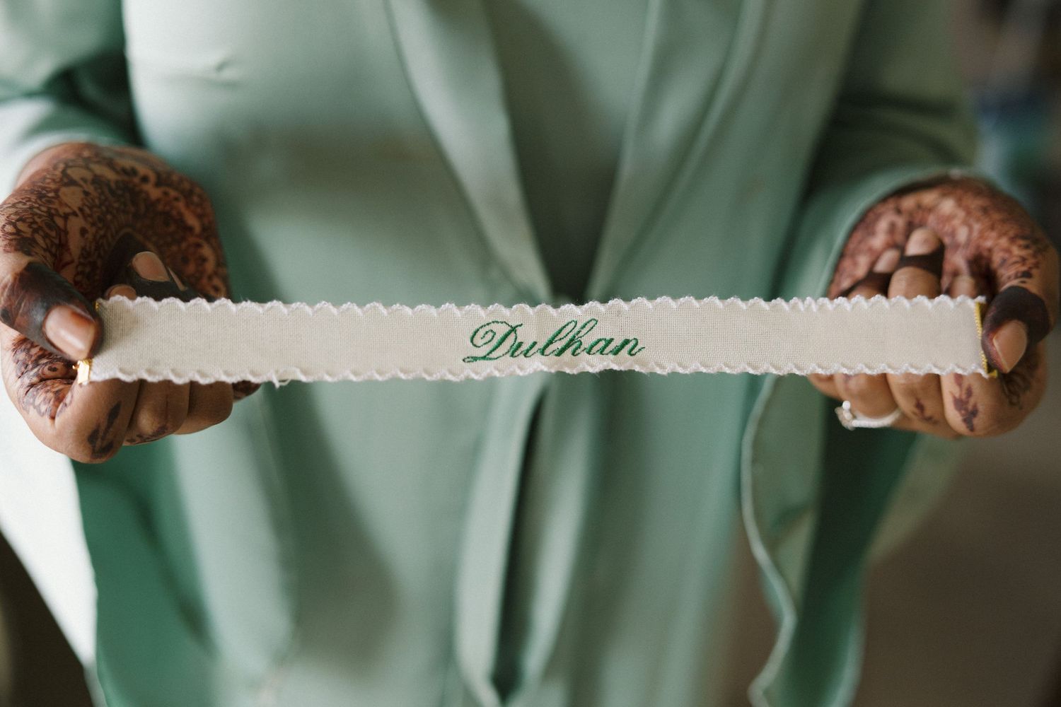 Bride holding a decorative white sash with the word Dulhan written in elegant green script.