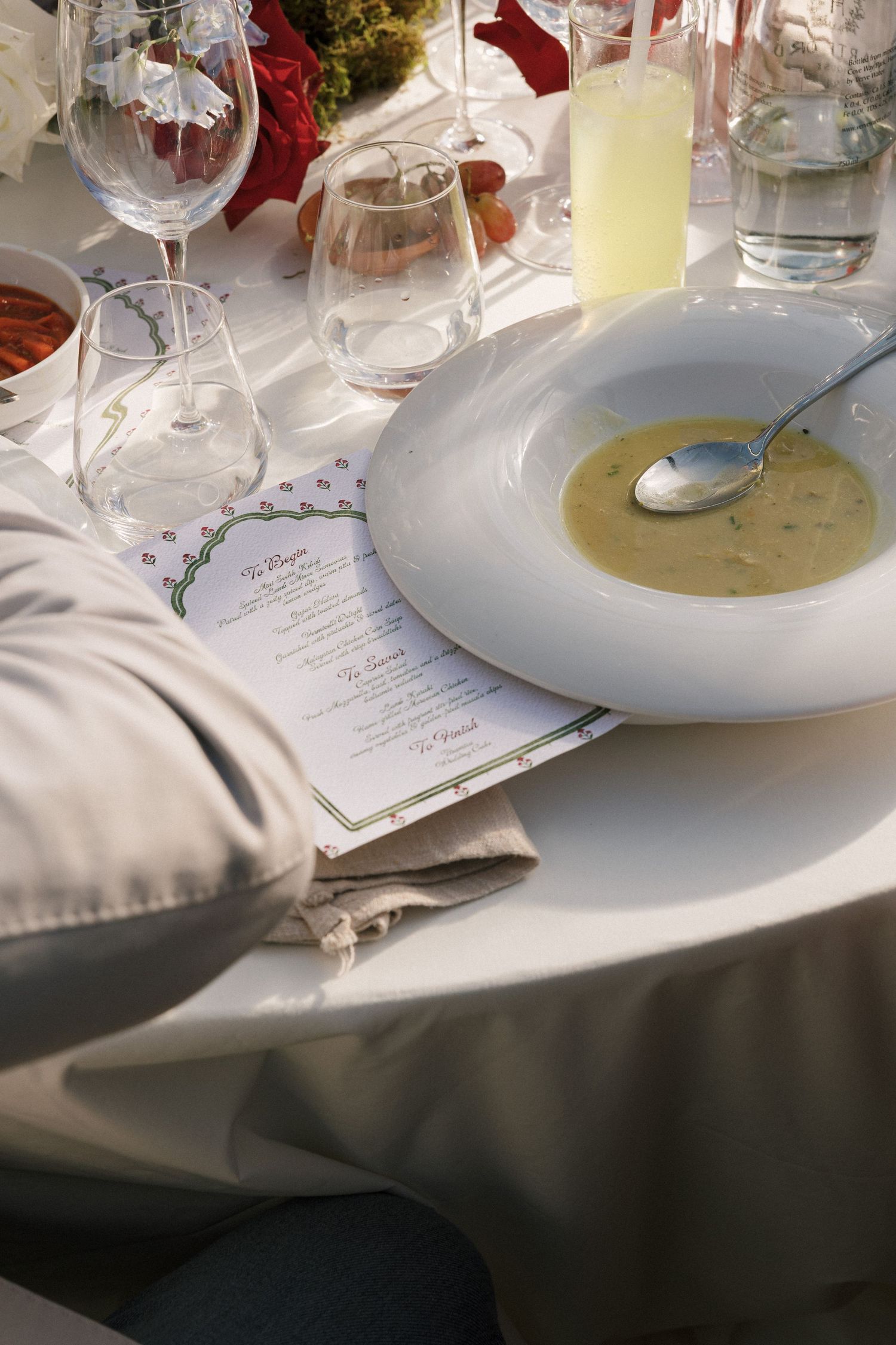 Elegant formal dining table setting with cream soup, wine glasses, menu card, and floral centerpiece at a catered event.