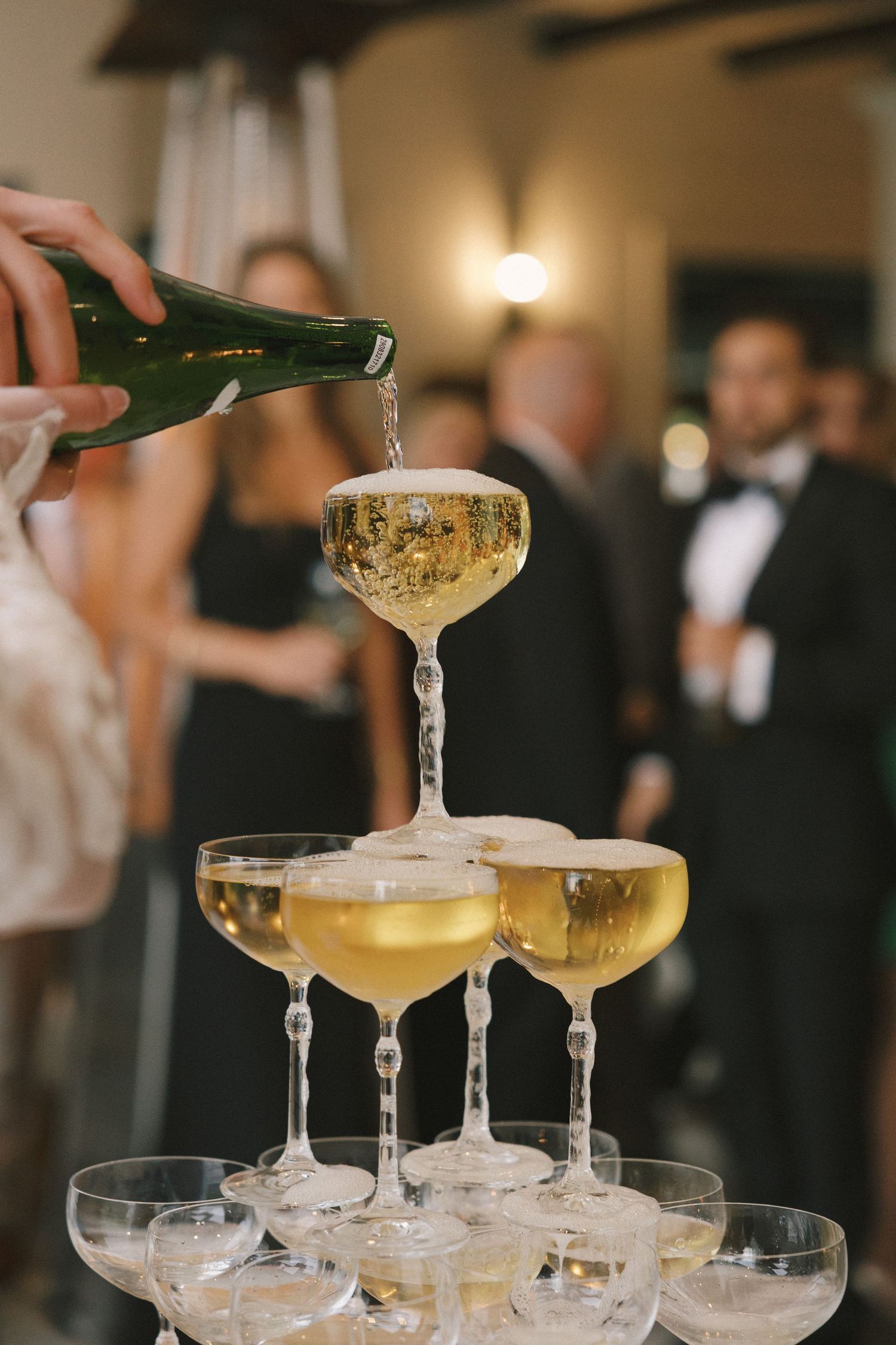 Champagne tower with golden bubbly being poured into delicate crystal coupe glasses at an elegant event.