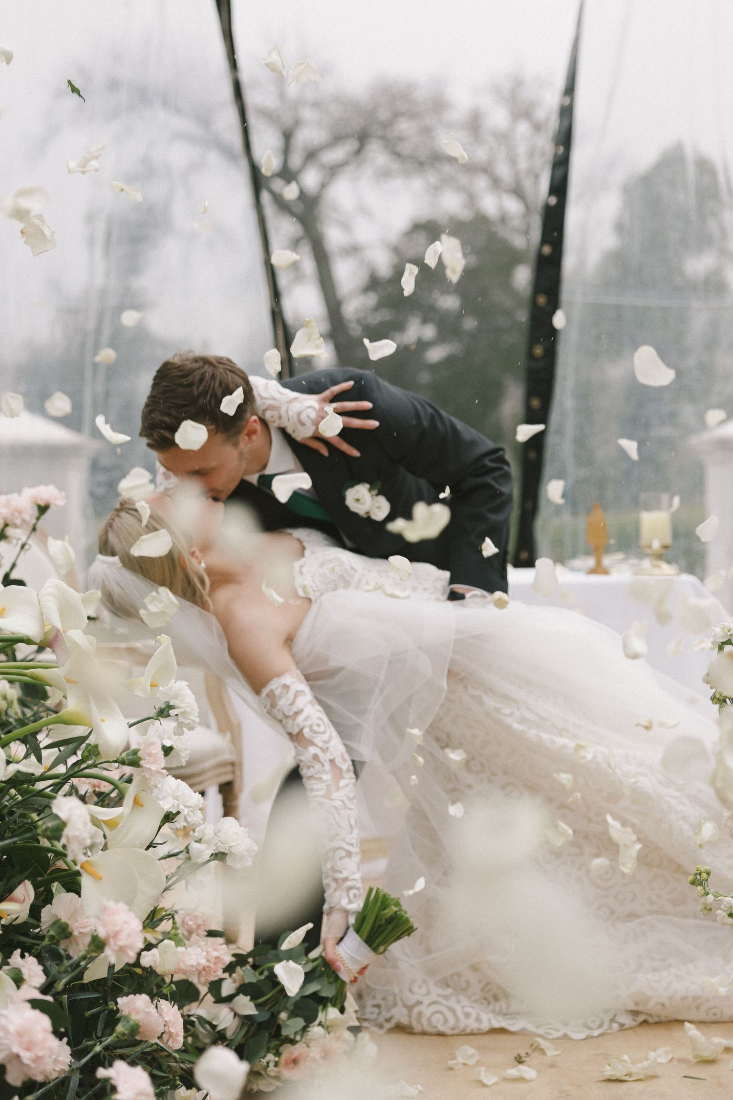 A dreamy wedding scene with flowing white gowns and flower petals creating an ethereal atmosphere outdoors.