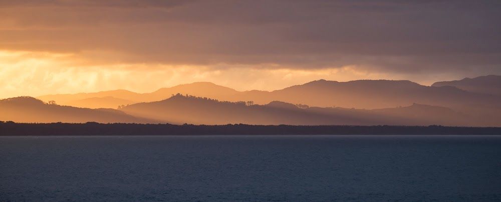 Stunning orange and gold sunset silhouetting mountain ranges over tranquil coastal ocean waters.