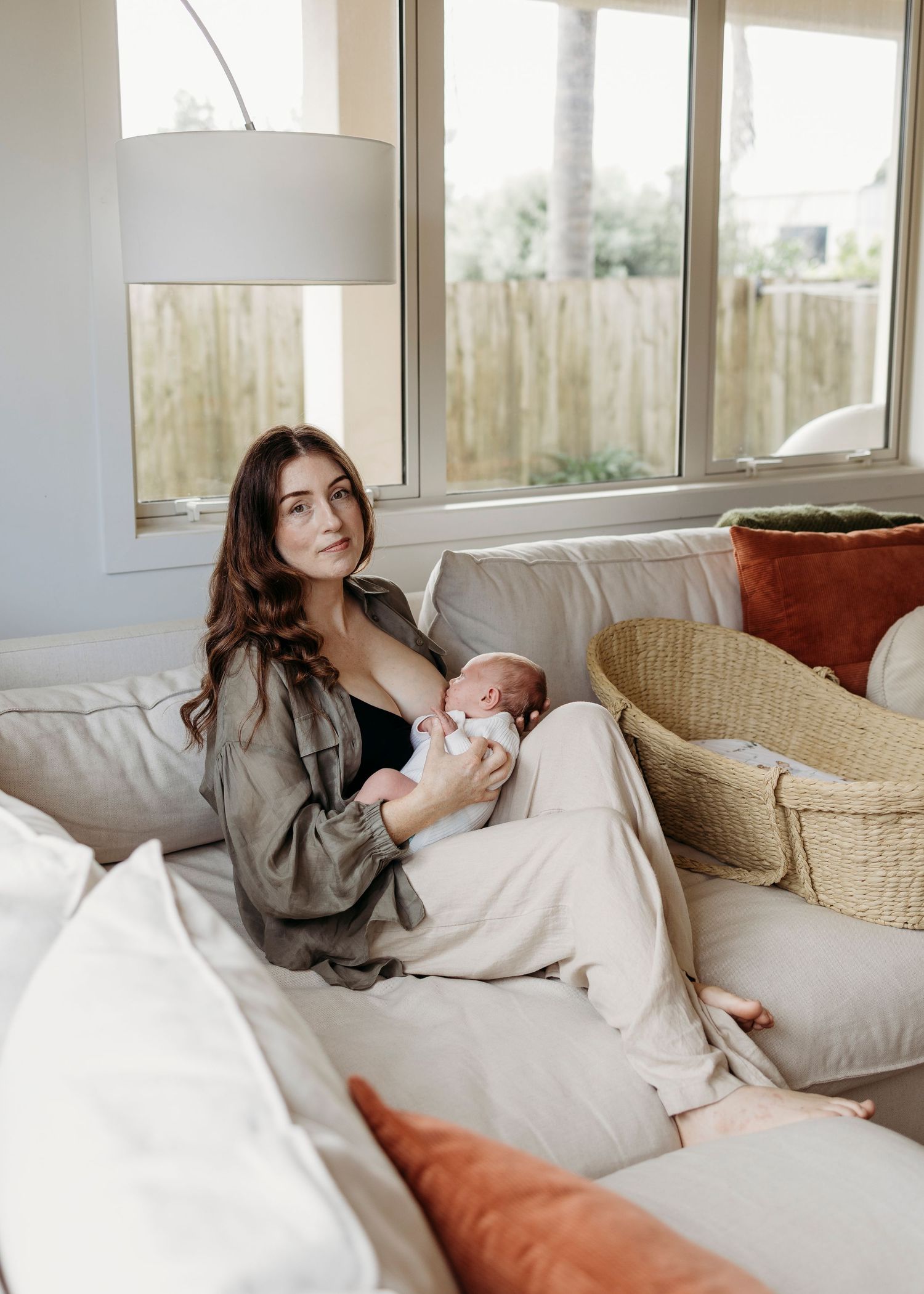 Brunette mother relaxing on sofa feeding her newborn baby near sunny windows.