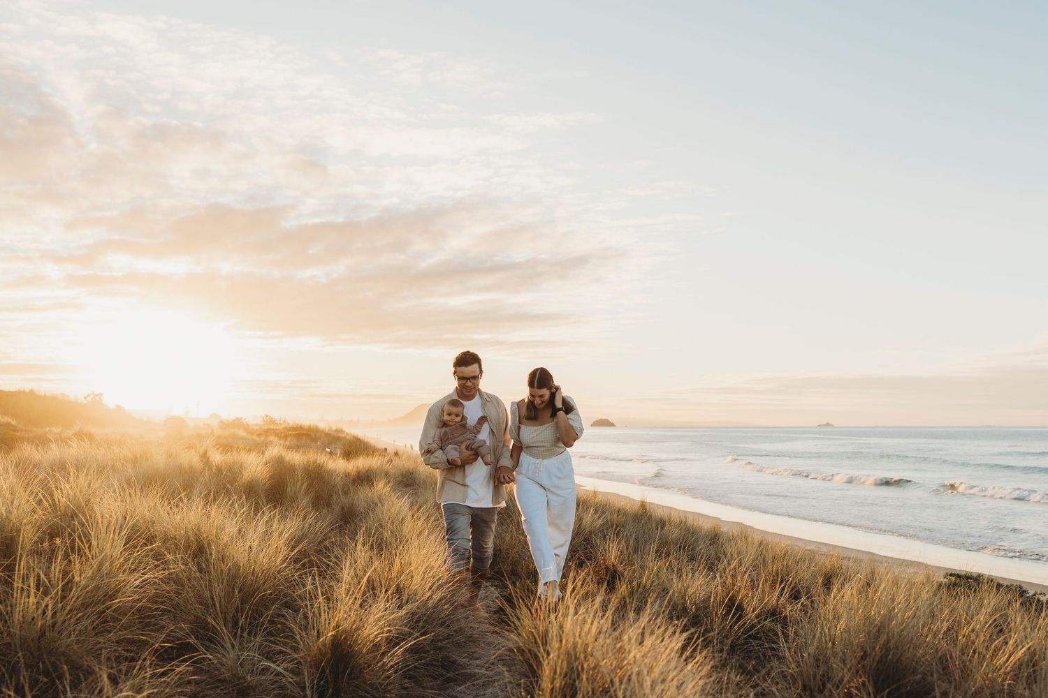 Young family walking on sandy beach path at golden sunset.