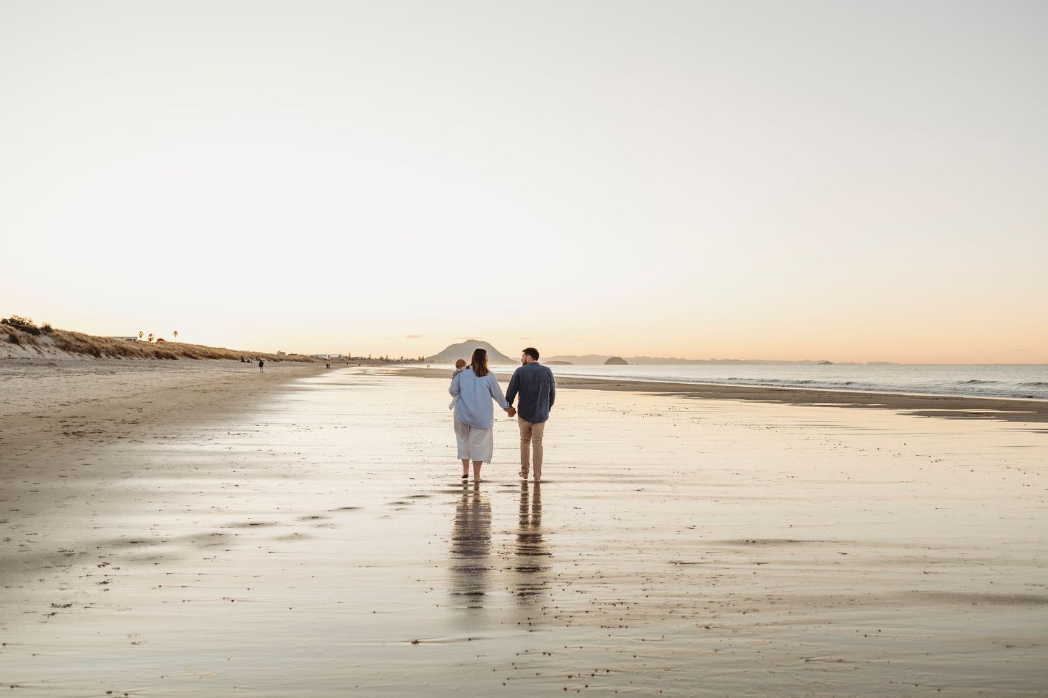 Couple holding hands walking along a serene beach at sunset with reflections on wet sand.