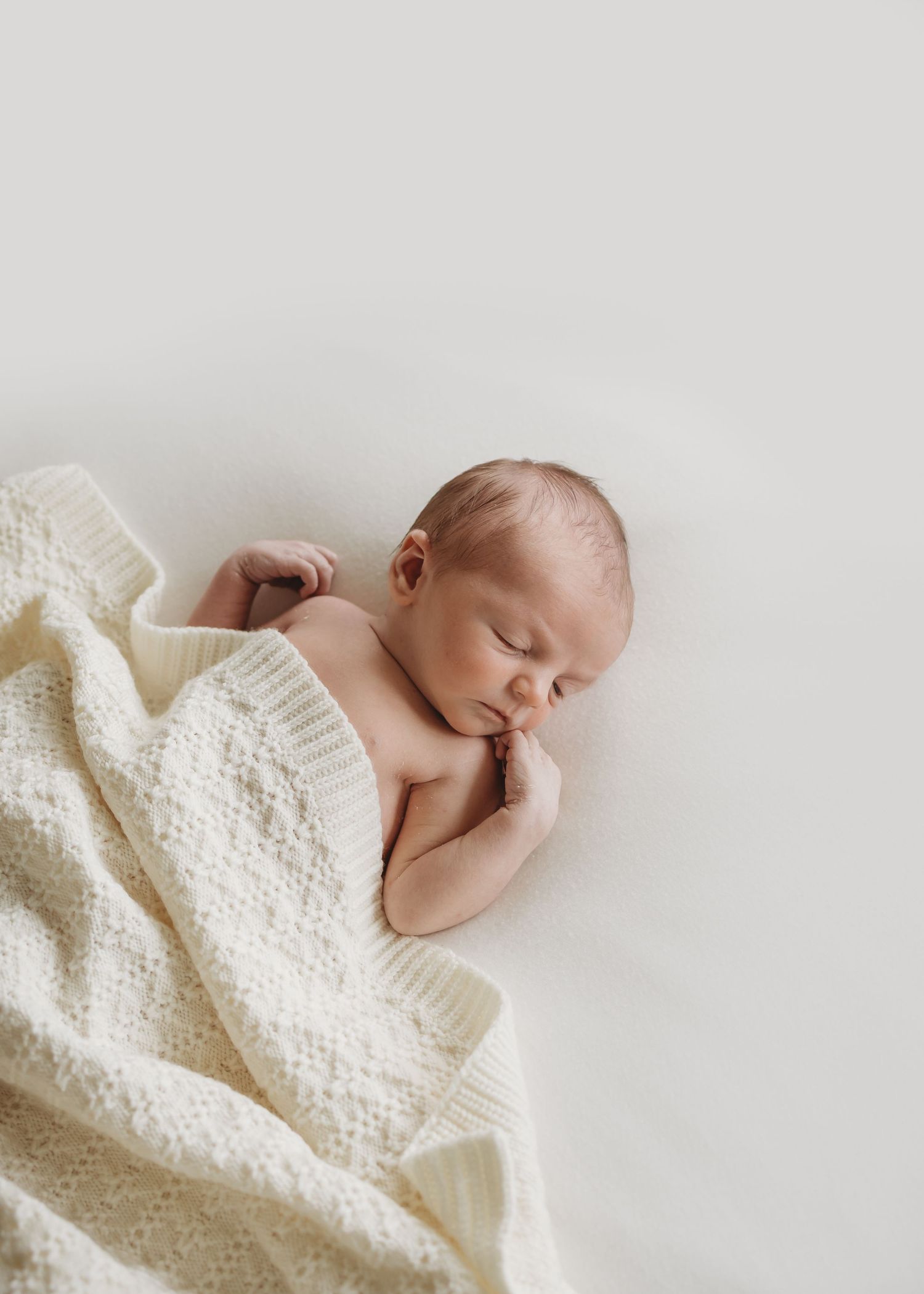 Sleeping newborn baby wrapped in a cream knit blanket on a white background.