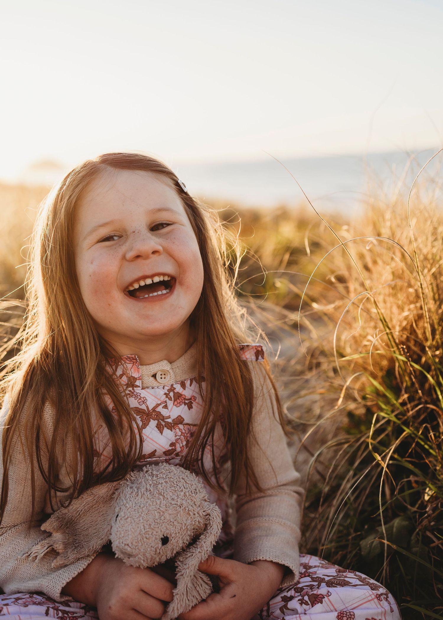 Happy young girl laughing in golden beach grass holding stuffed bunny.