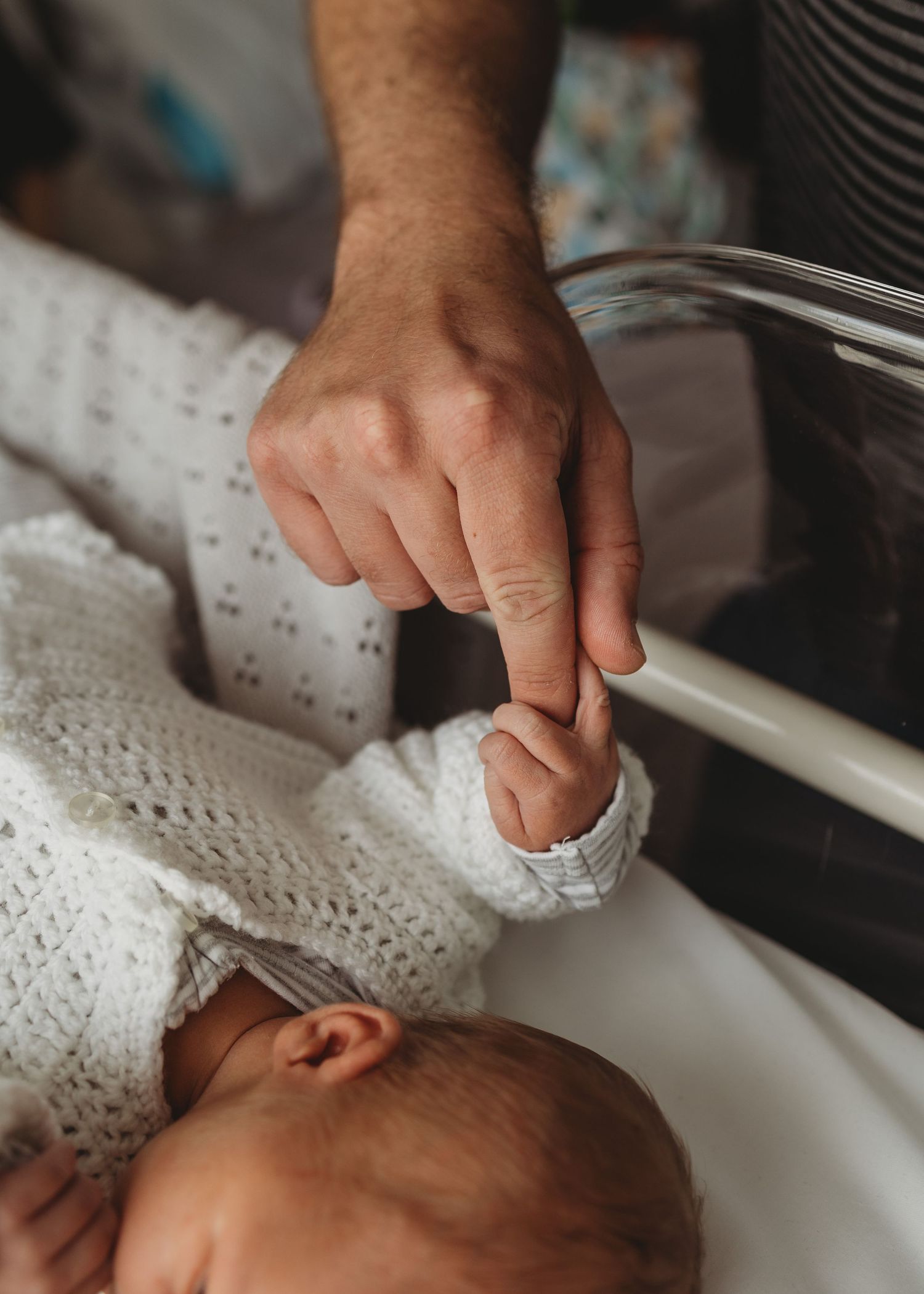 Newborn baby grasping fathers finger in hospital crib.