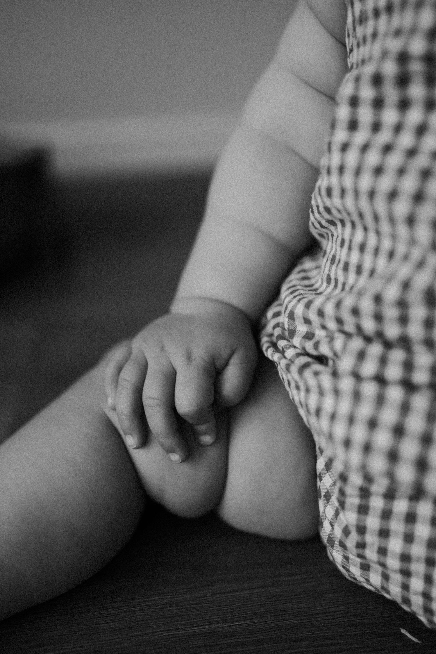Close-up black and white photo of a baby's chubby hand resting on their leg wearing a checkered outfit.