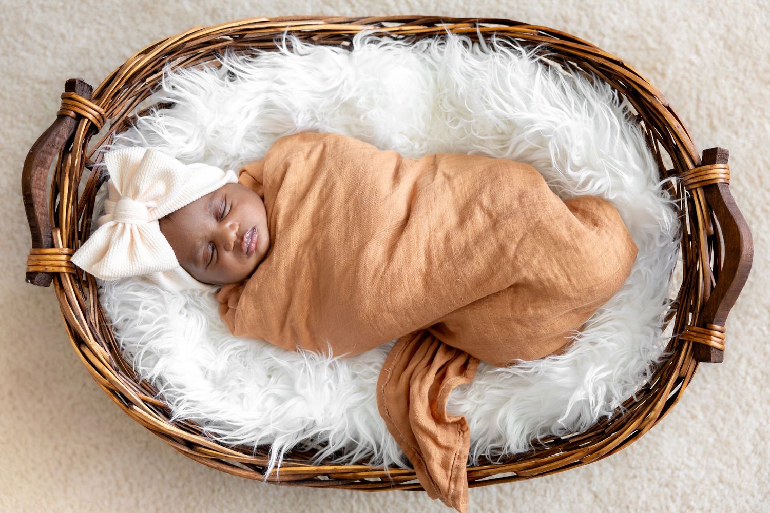 Newborn baby sleeping peacefully in woven basket lined with white fur.