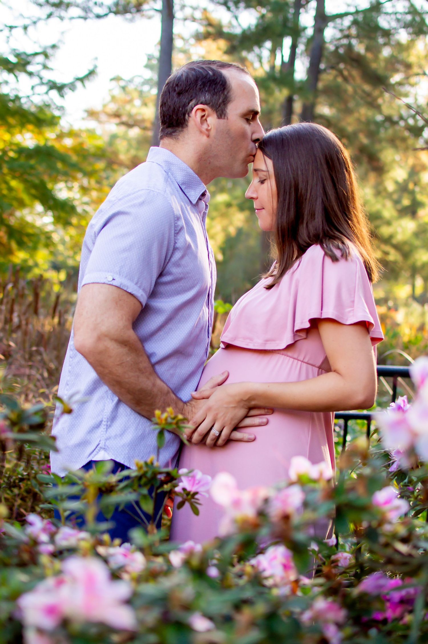 Couple embraces in a garden setting with pink flowers blooming around them.