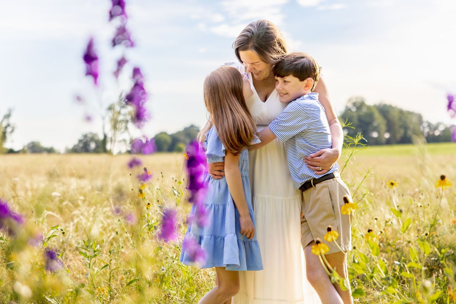 A tender family moment in a wildflower field with purple delphiniums at sunset at Blue Hill Garden in Monroe, NC.