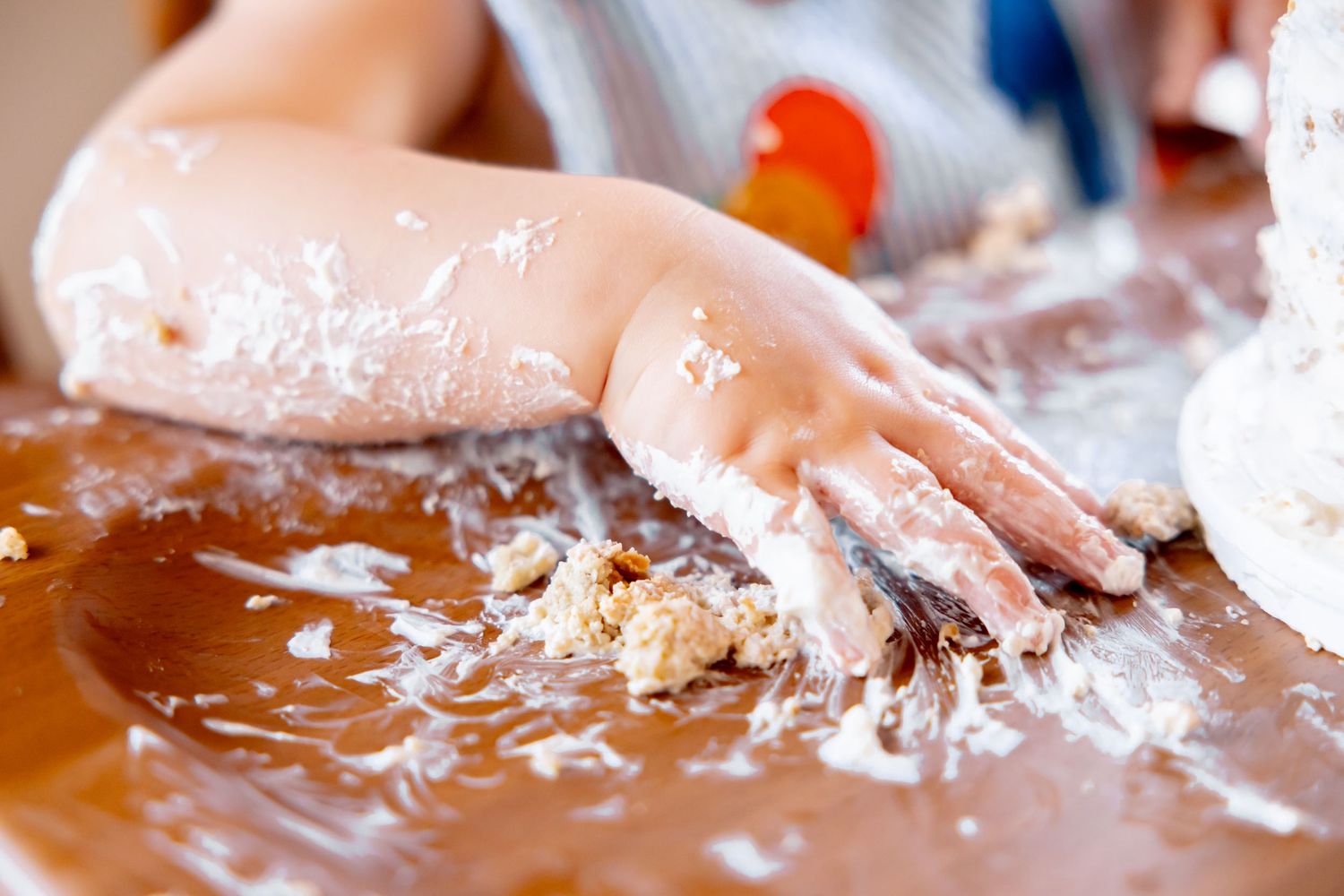 Messy cake smashing scene with tiny hands playing in frosting.