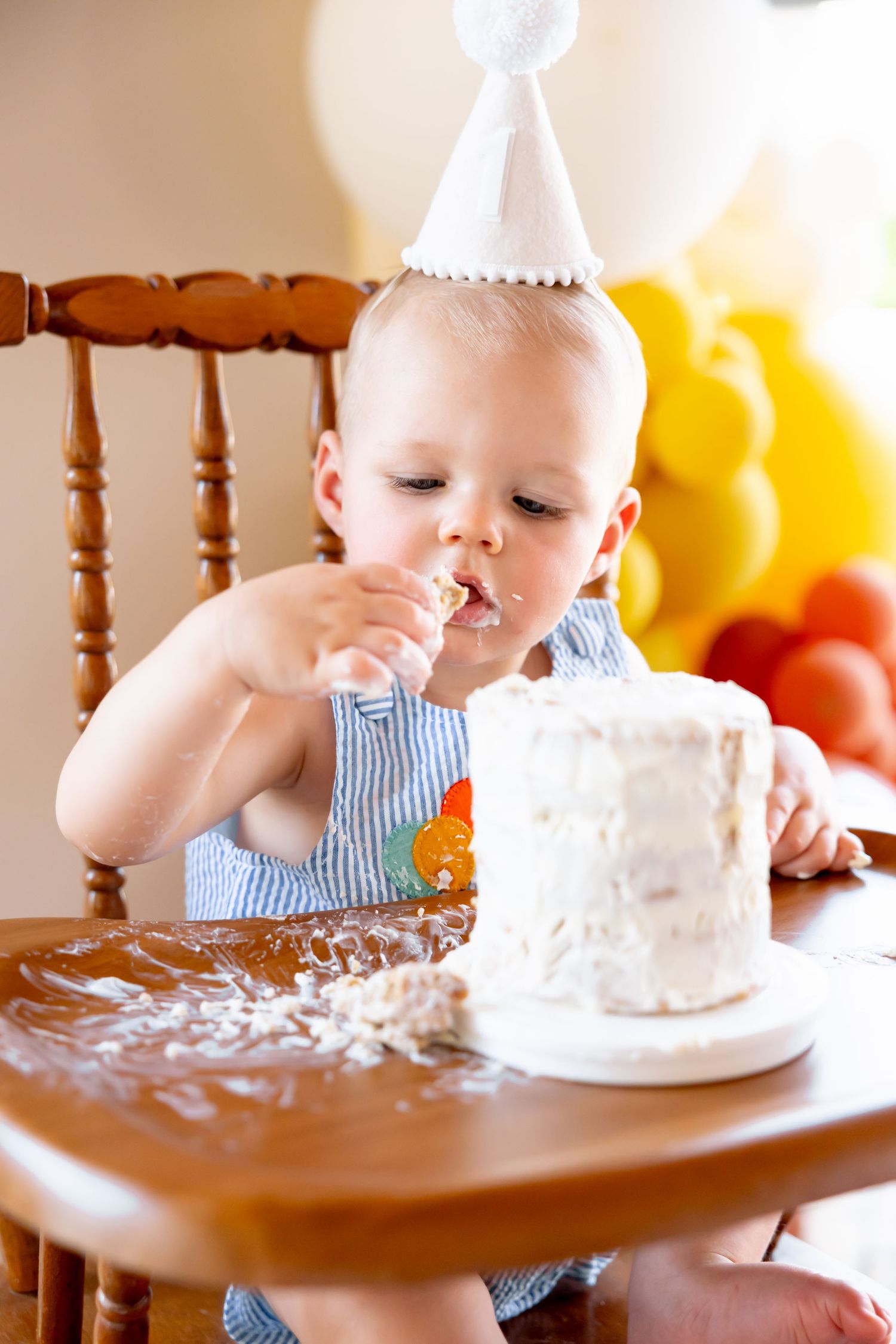 First birthday cake smash scene with white cake on vintage wooden high chair.