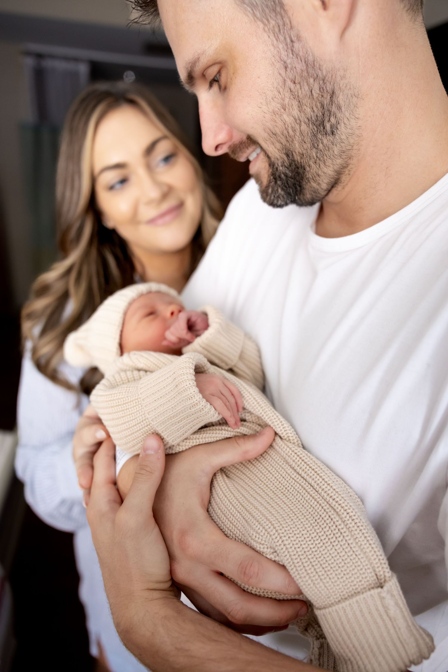 New parents lovingly gaze at their newborn baby wrapped in a cozy beige knit blanket.