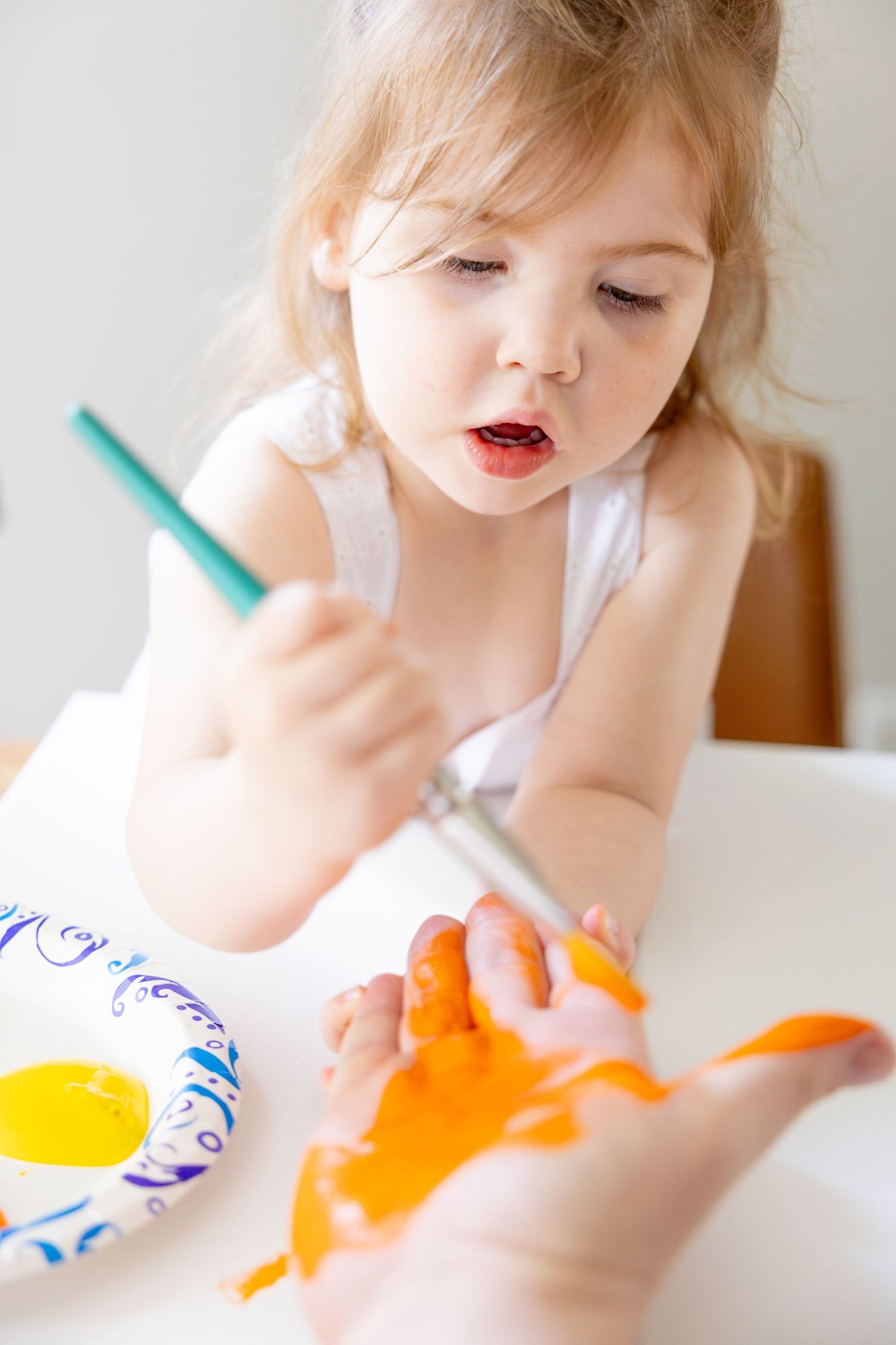 Child concentrating on painting activity with orange paint and art supplies.