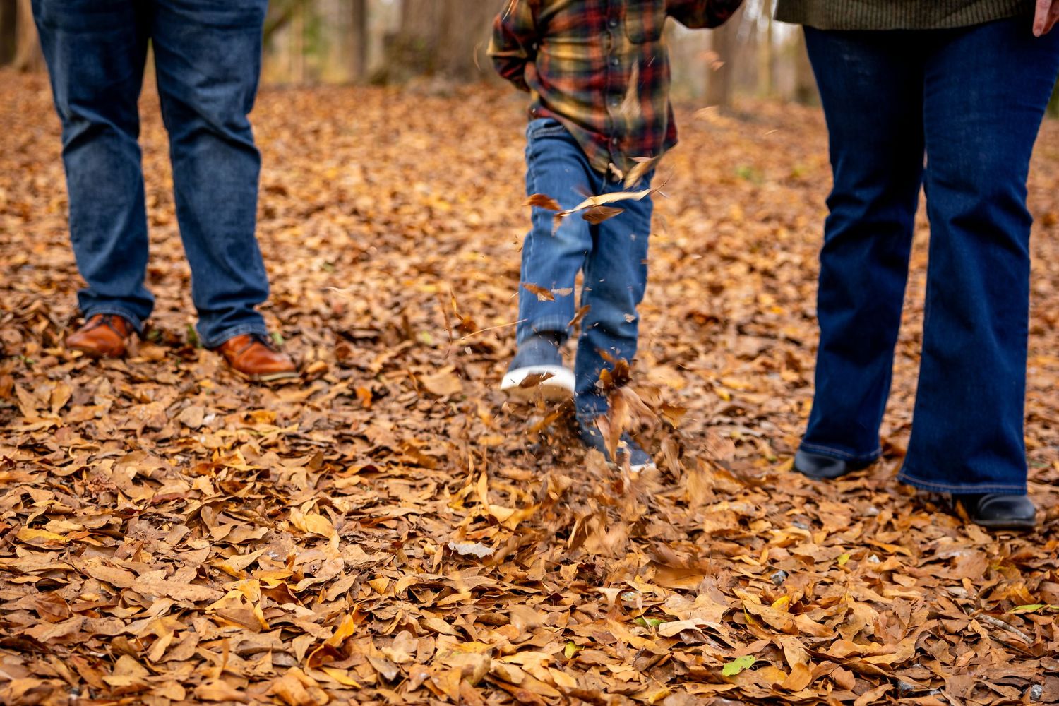 Close-up of feet walking through crisp autumn leaves during an outdoor family photoshoot.