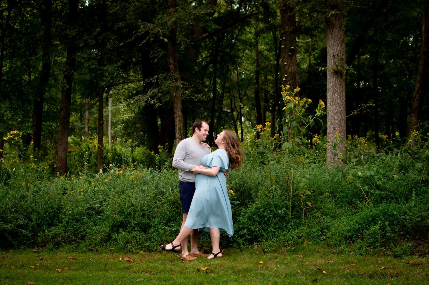 A couple dancing together in a wooded area with golden sunlight.