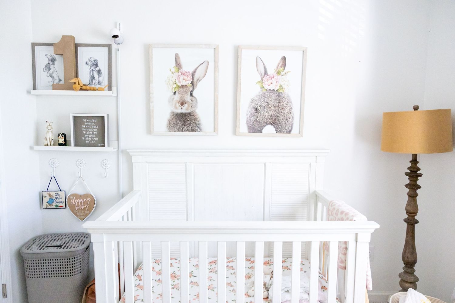 Modern nursery with white crib, wooden shelves, and framed bunny artwork on walls.