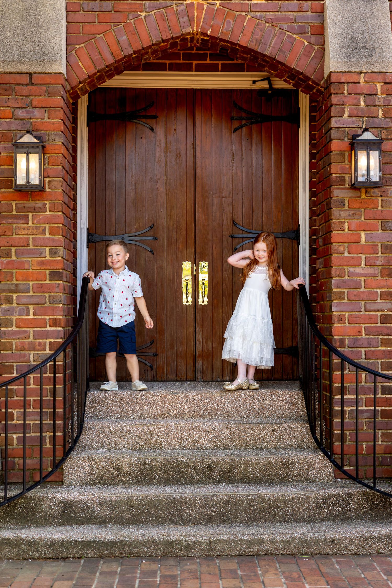 Sequence of children in white outfits playing on brick church steps with wooden doors.