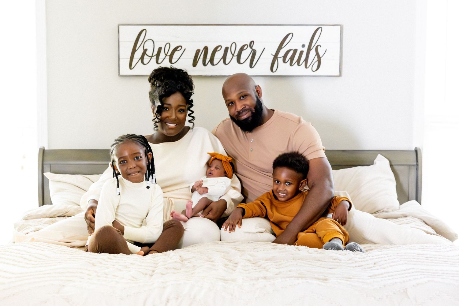 A cozy bedroom interior with white bedding and a 'love never fails' sign on the wall.