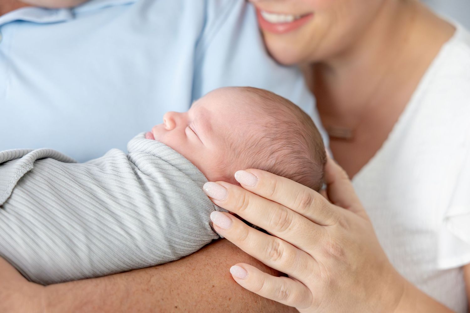 Tender moment with parents holding newborn swaddled in grey blanket during lifestyle newborn session.