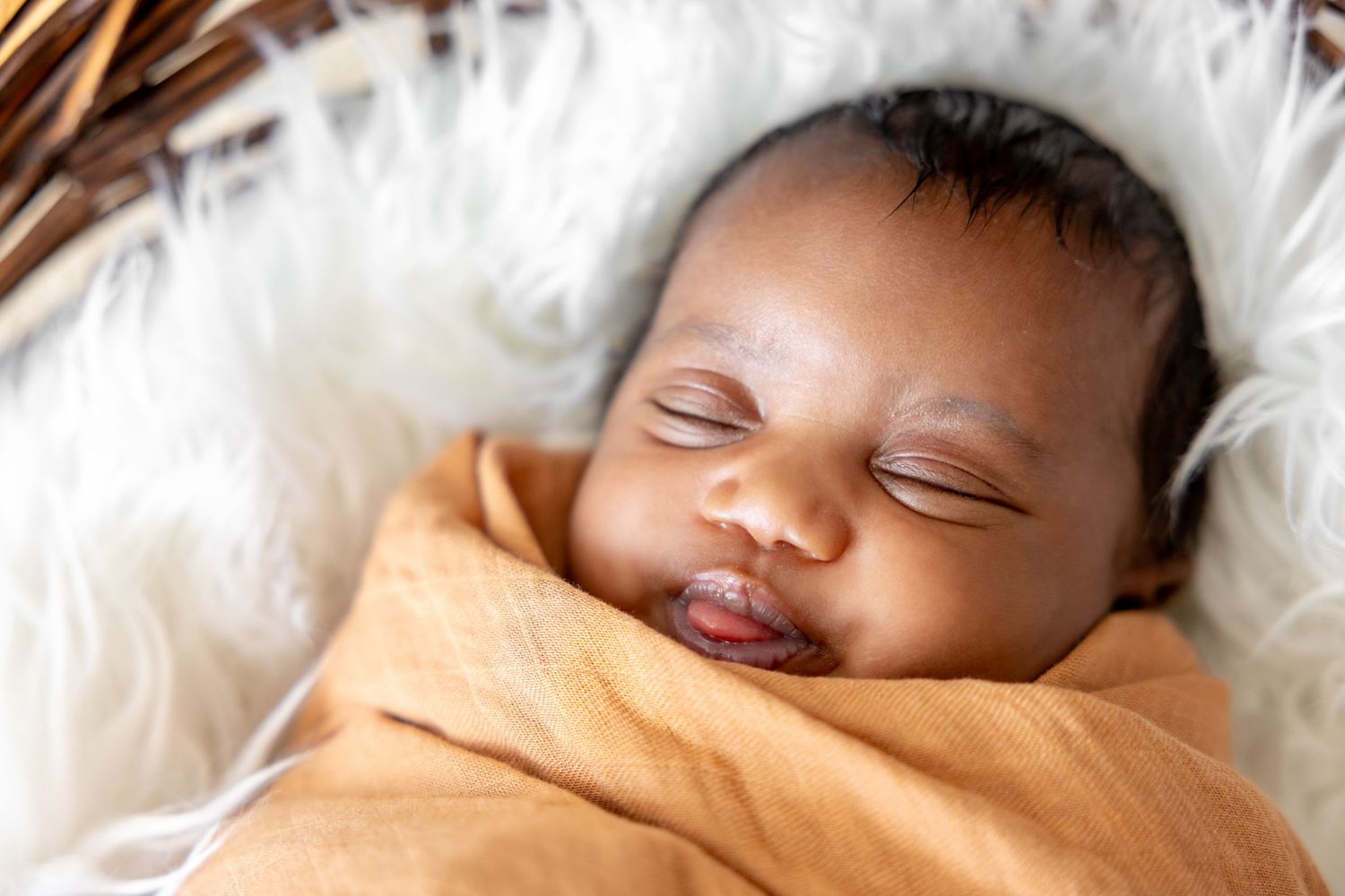 Sleeping newborn wrapped in orange blanket against white fur background.