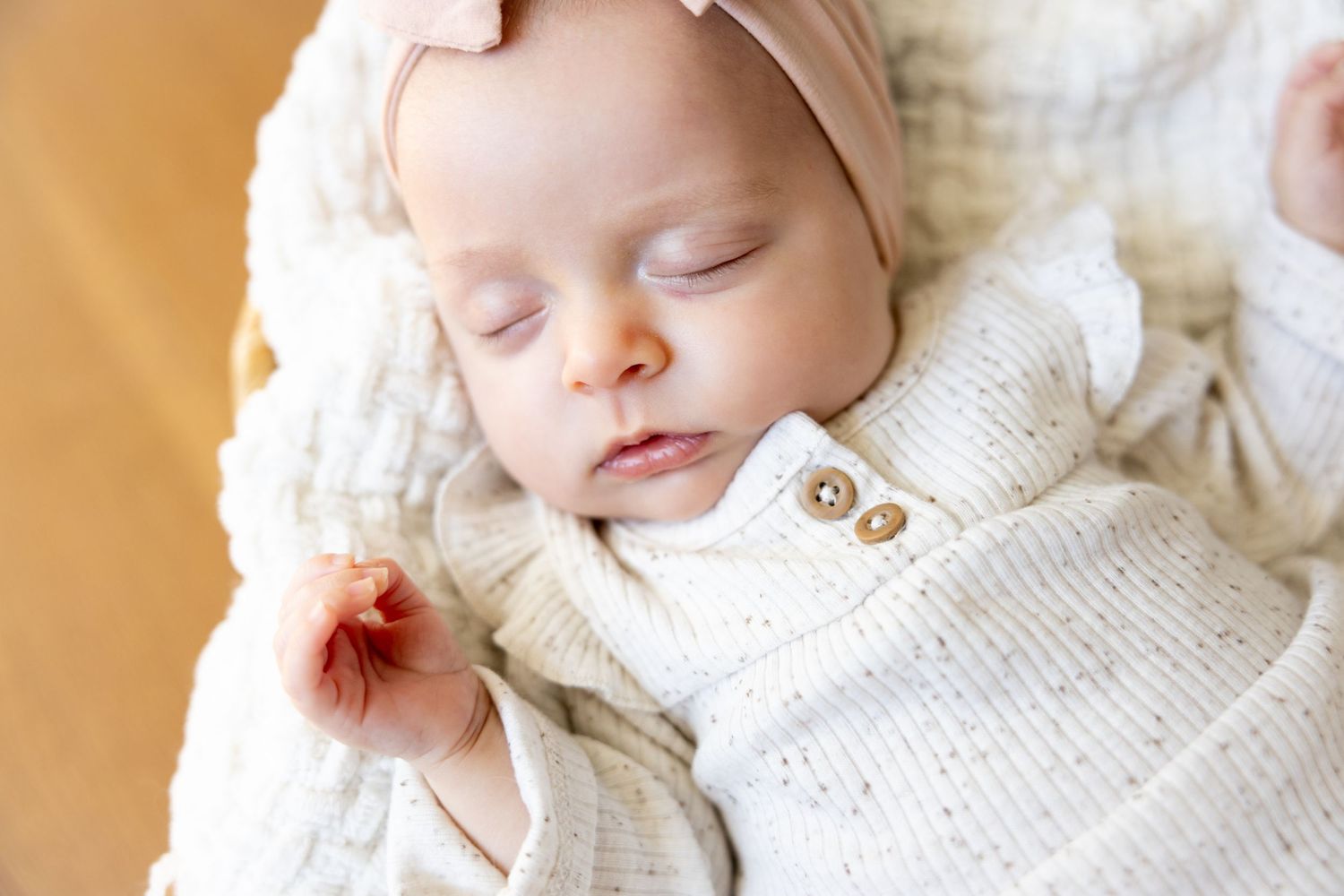 A sleeping baby wearing a white knit sweater and beige headband.